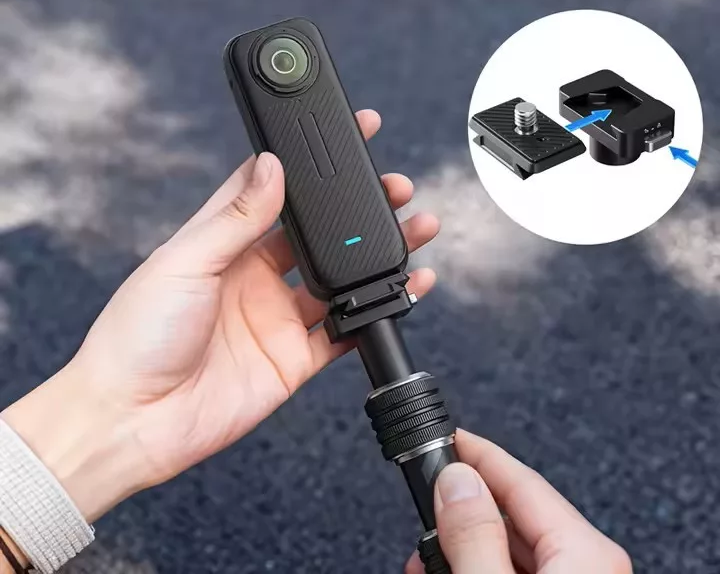 Fekete 360 fokos akciókamerát szelfibottal tartó kezek, a rögzítési mechanizmust mutató betéttel.