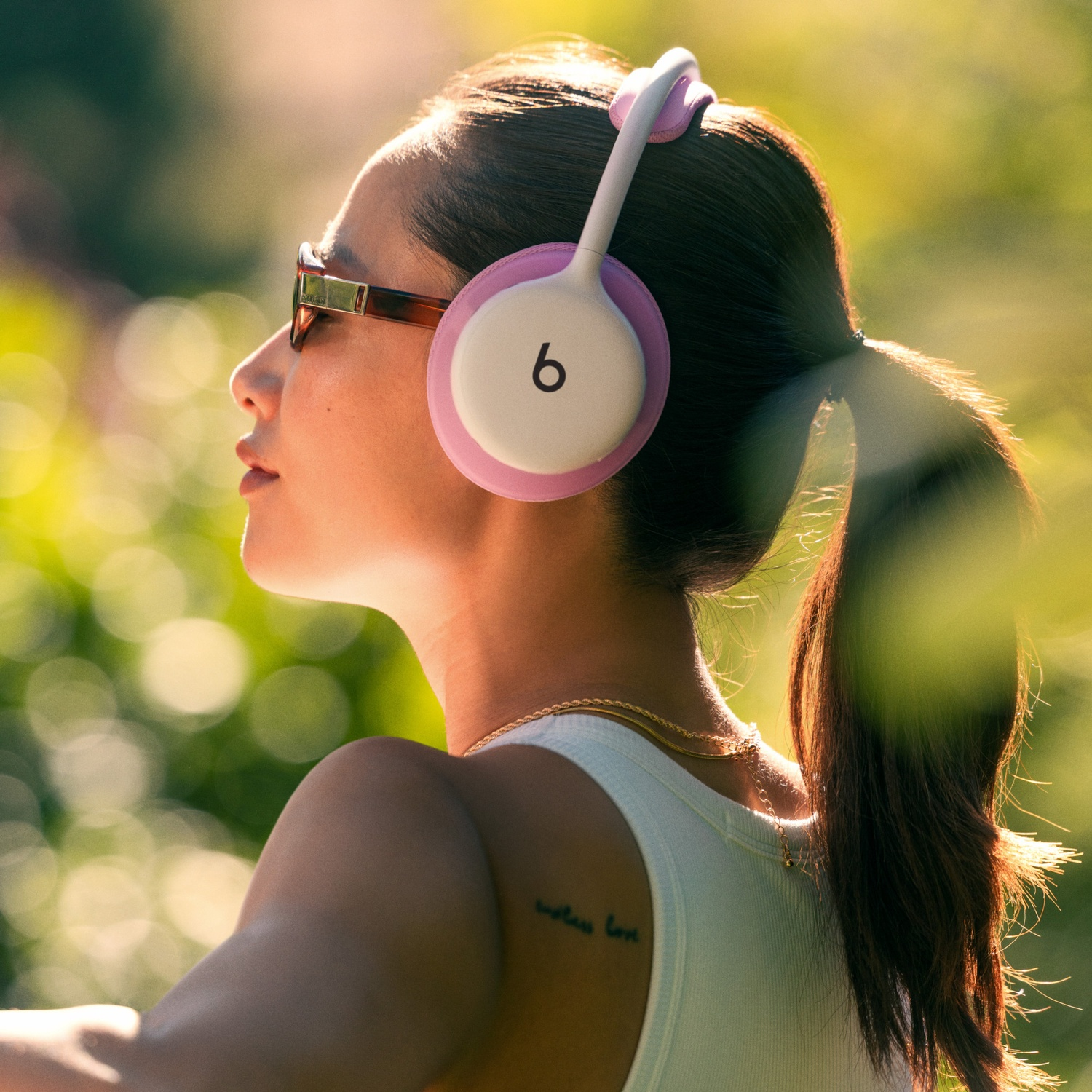 Une femme de profil porte un casque Beats blanc et rose et des lunettes de soleil au soleil.