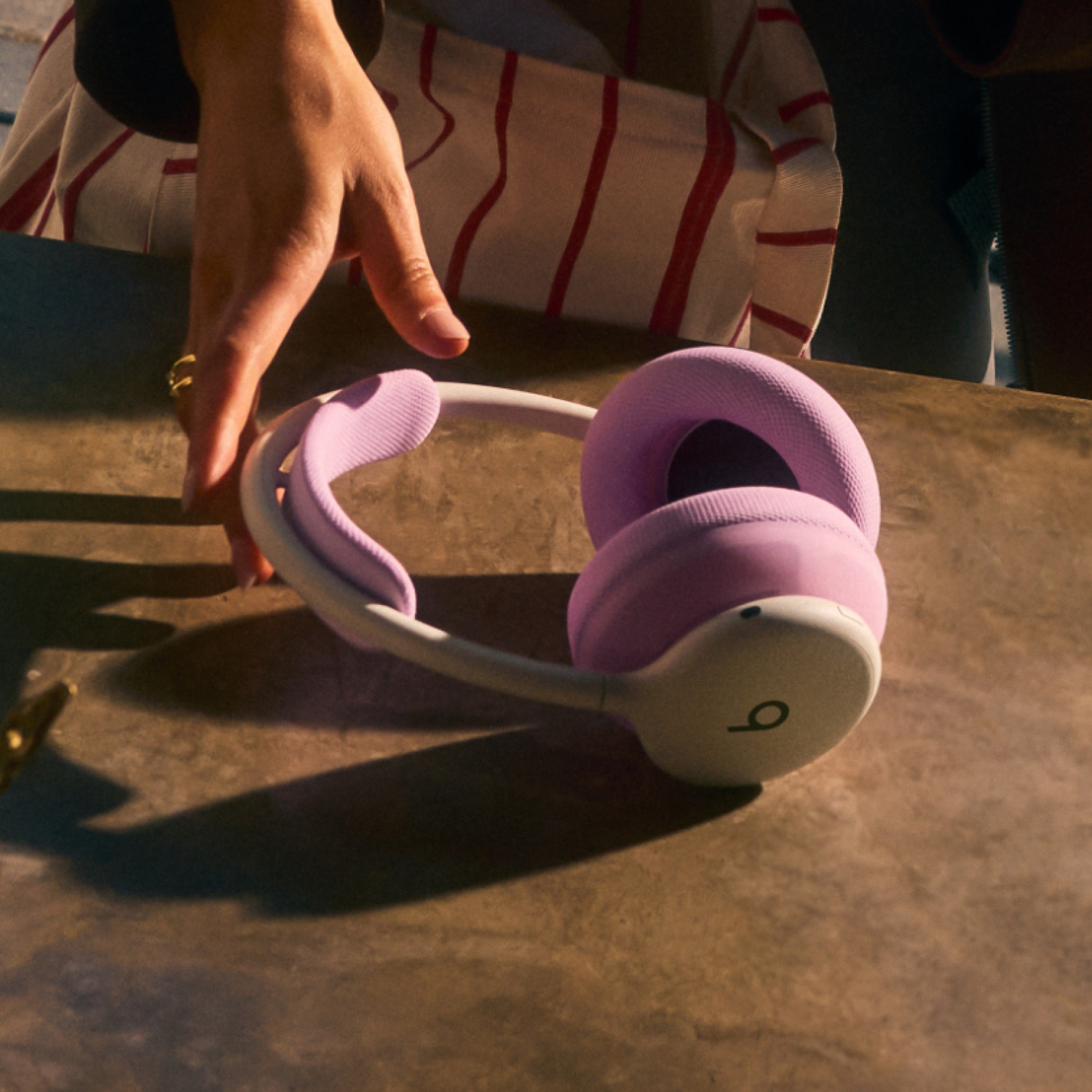 Une main attrape un casque audio rose et blanc sur une table.