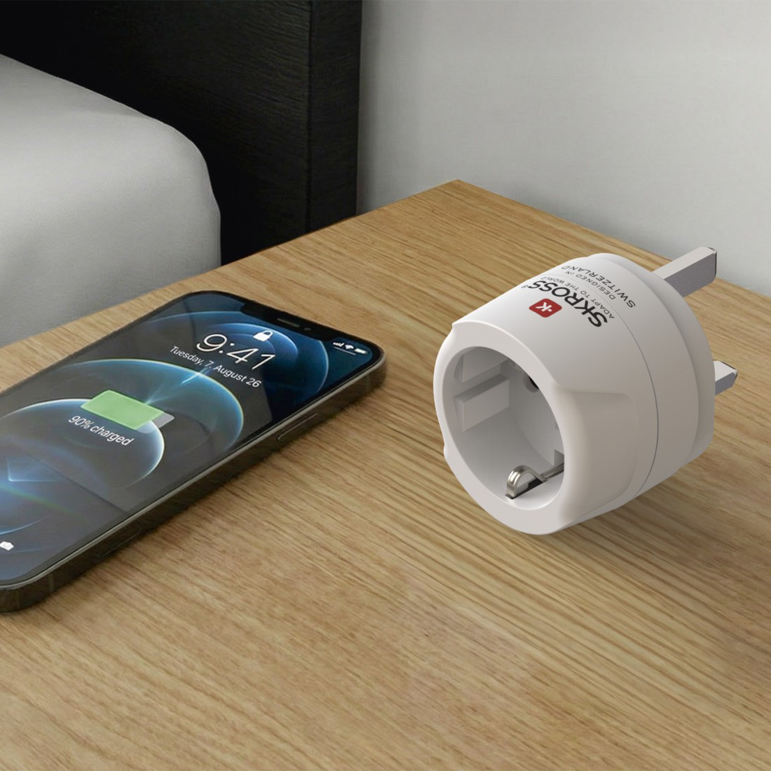 Un adaptador de viaje Skross blanco y un smartphone en una mesita de noche de madera.