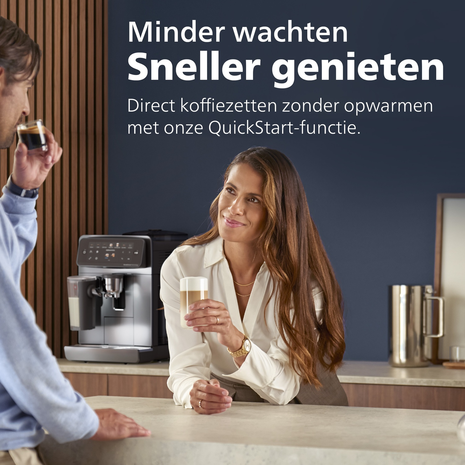 A woman holds a latte macchiato glass and looks at a man drinking coffee, near a coffee machine.
