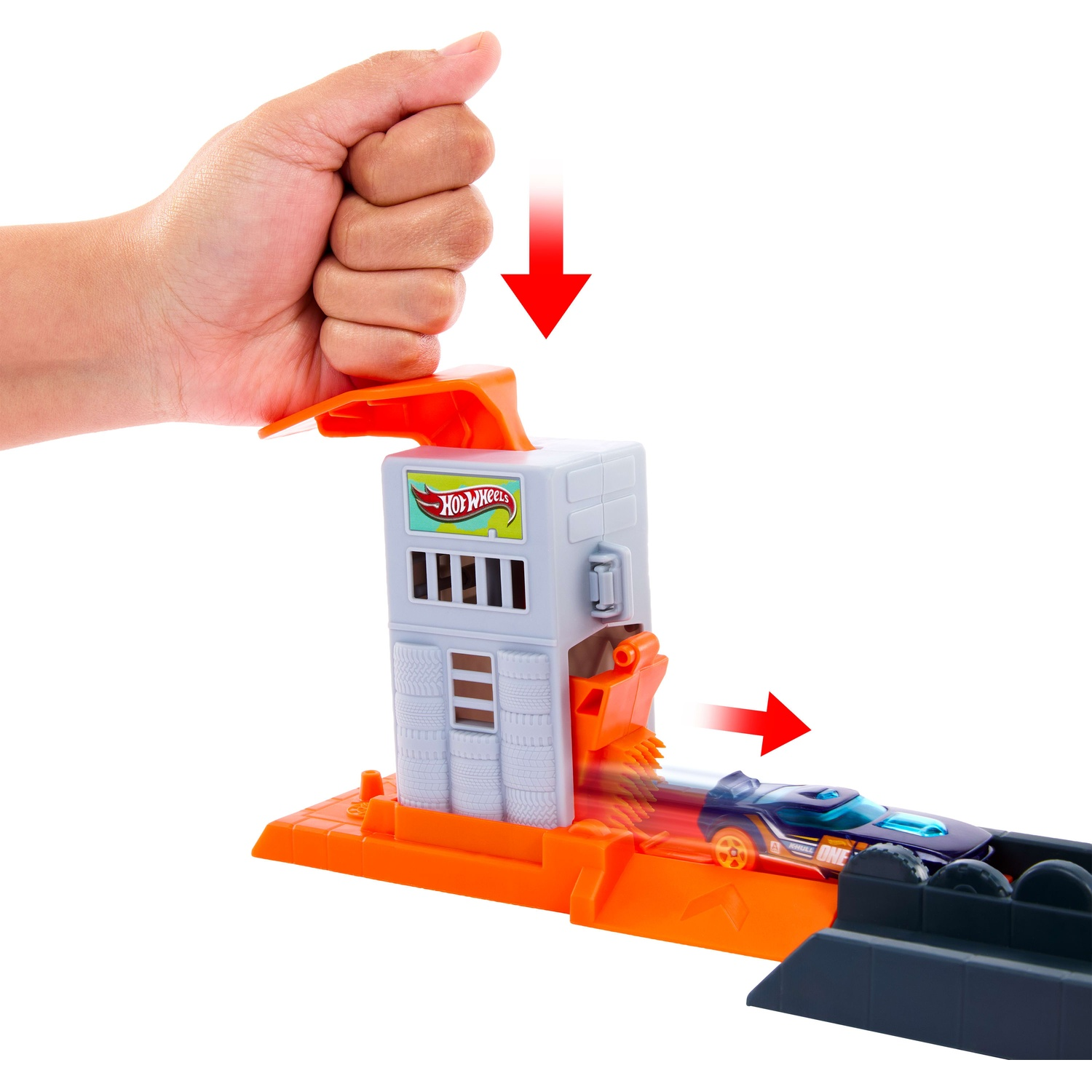 A hand presses down on a Hot Wheels launcher, sending a toy car speeding forward.