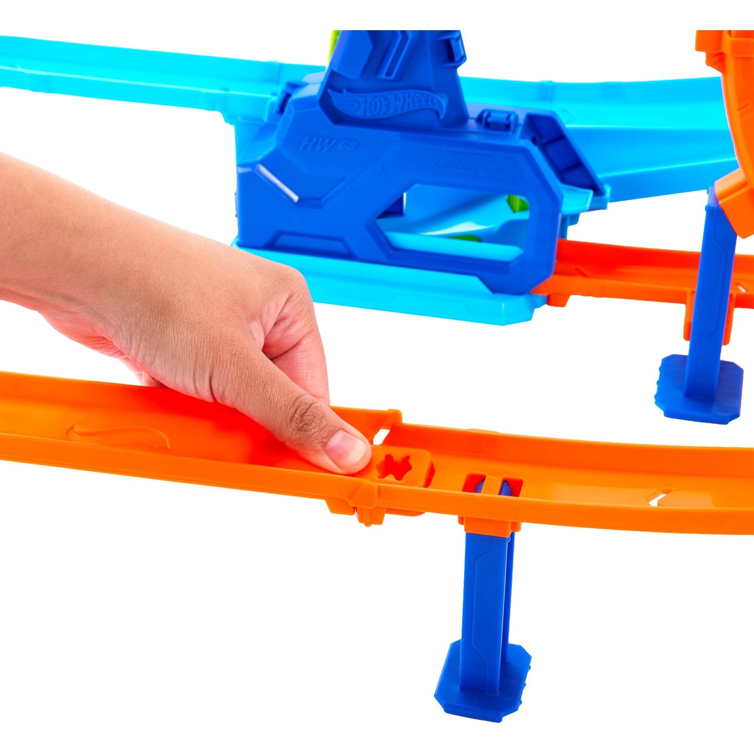 A hand connects orange Hot Wheels track pieces in front of a blue and orange playset.