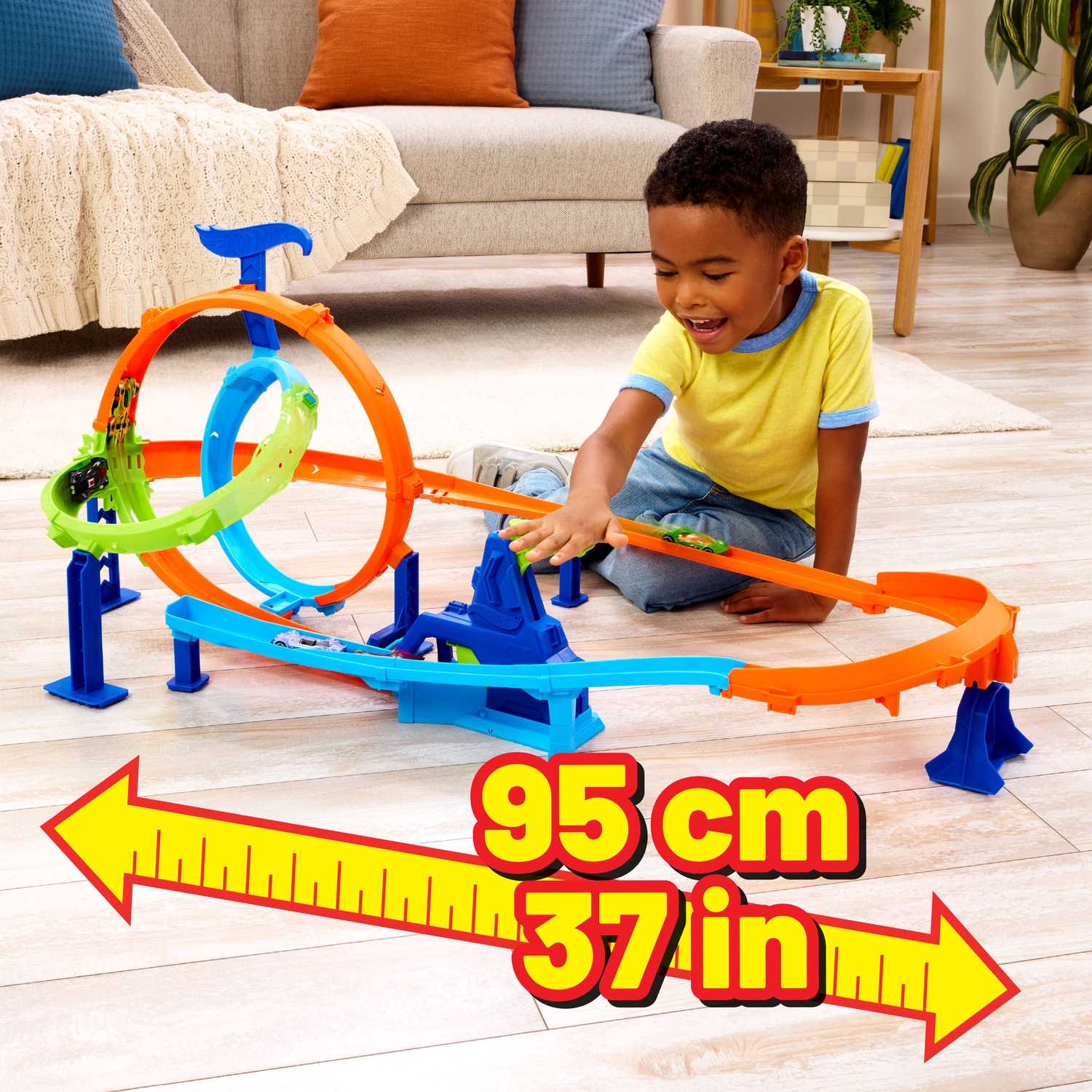 A boy sits on the floor playing with a large colorful toy race track that is 95 cm wide.