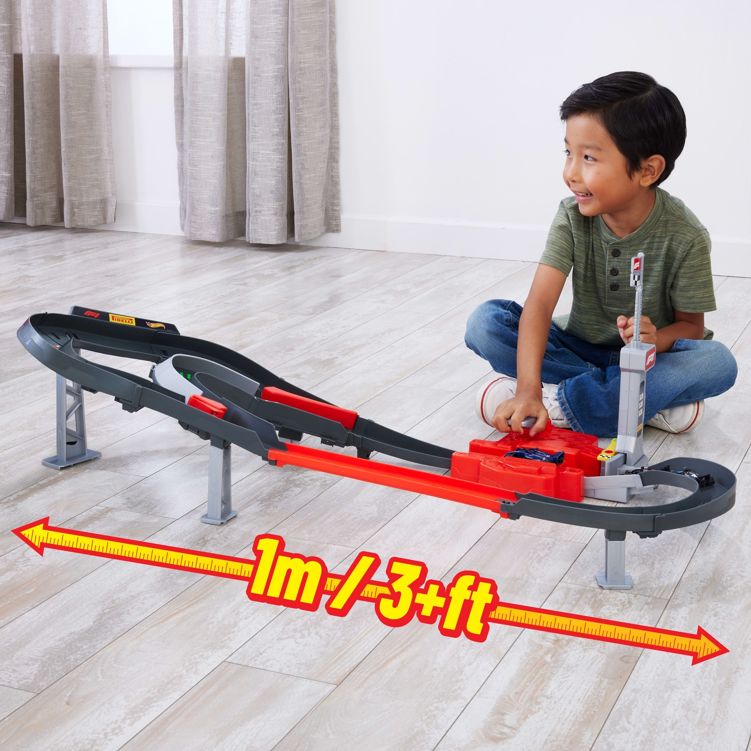 A boy sits on a wooden floor, playing with a large toy racetrack.