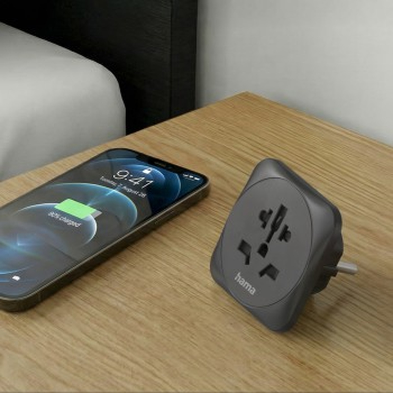 Een smartphone en een grijze reisstekker liggen op een houten tafel.