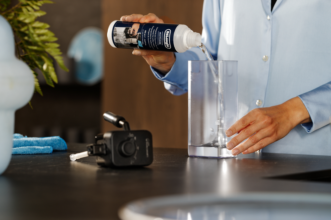 Eine Person gießt Reinigungsmittel aus einer DeLonghi-Flasche in einen klaren Wasserbehälter.