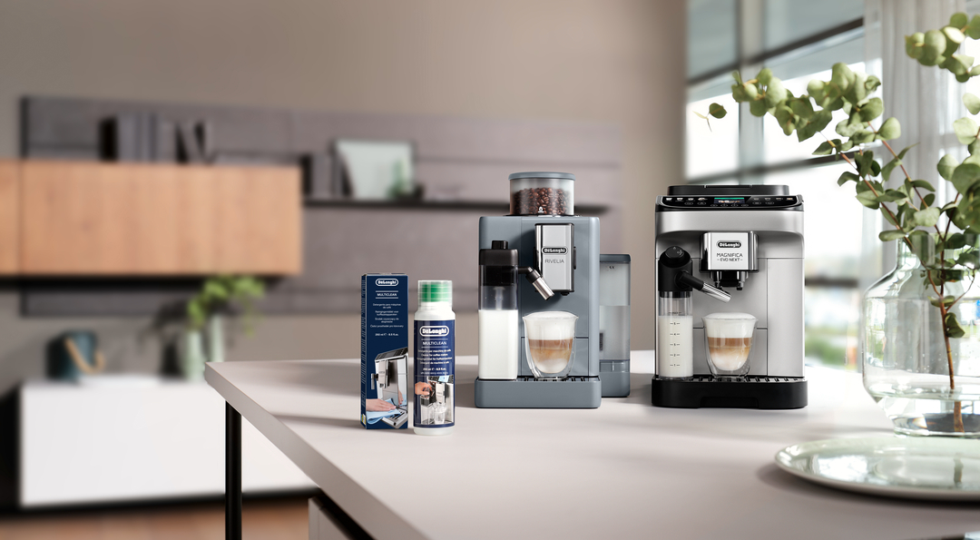 Zwei Kaffeemaschinen und eine Reinigungsflüssigkeit stehen auf einem weißen Tisch vor einer Küche.