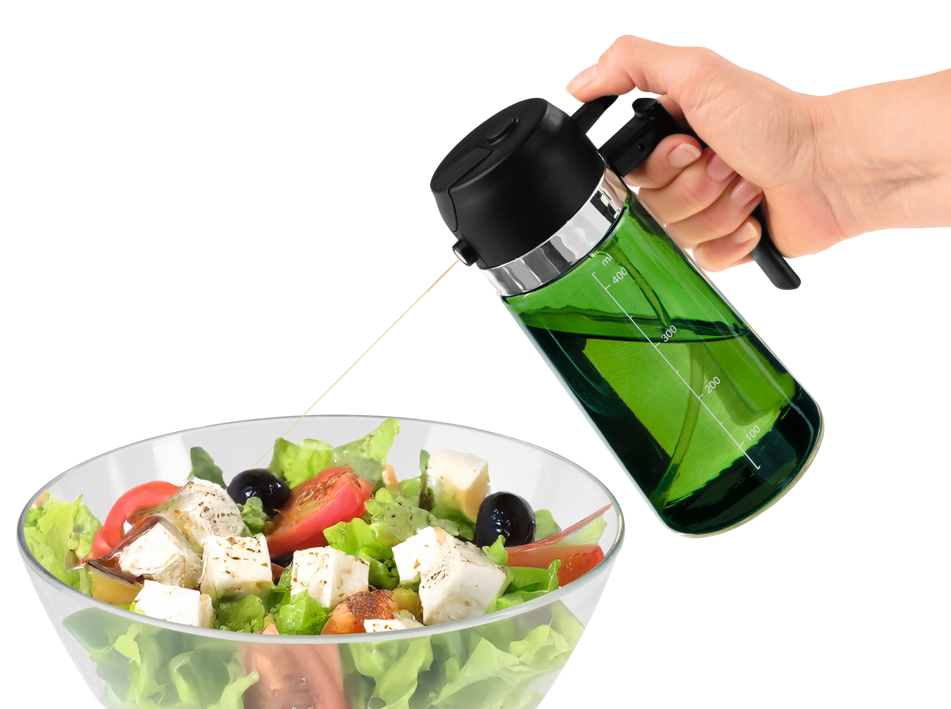 Eine Hand gießt Olivenöl aus einer grünen Glasflasche über einen griechischen Salat in einer Glasschüssel.