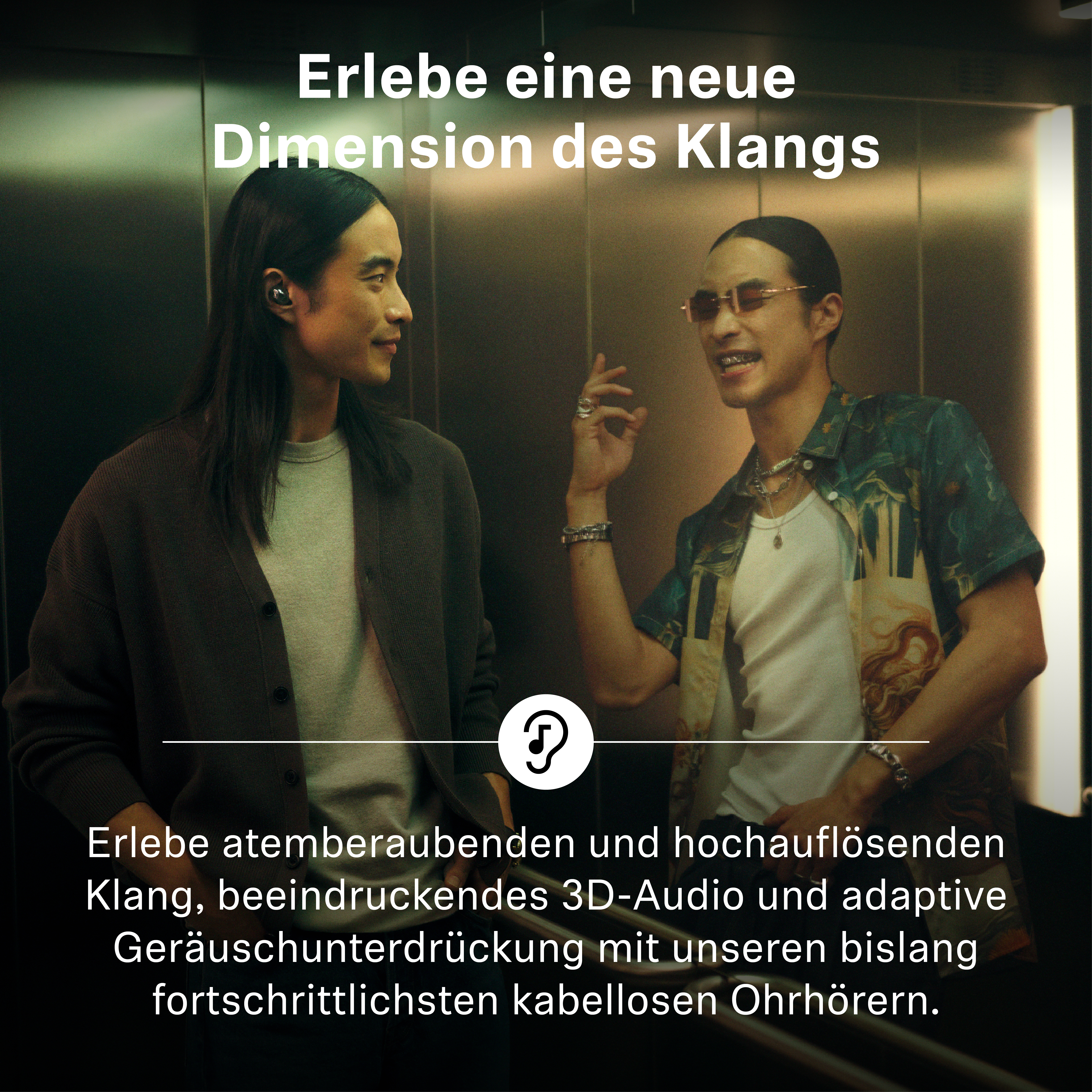 Zwei Männer im Aufzug, einer mit langen Haaren und dunkler Strickjacke, der andere mit Brille und gemustertem Hemd.