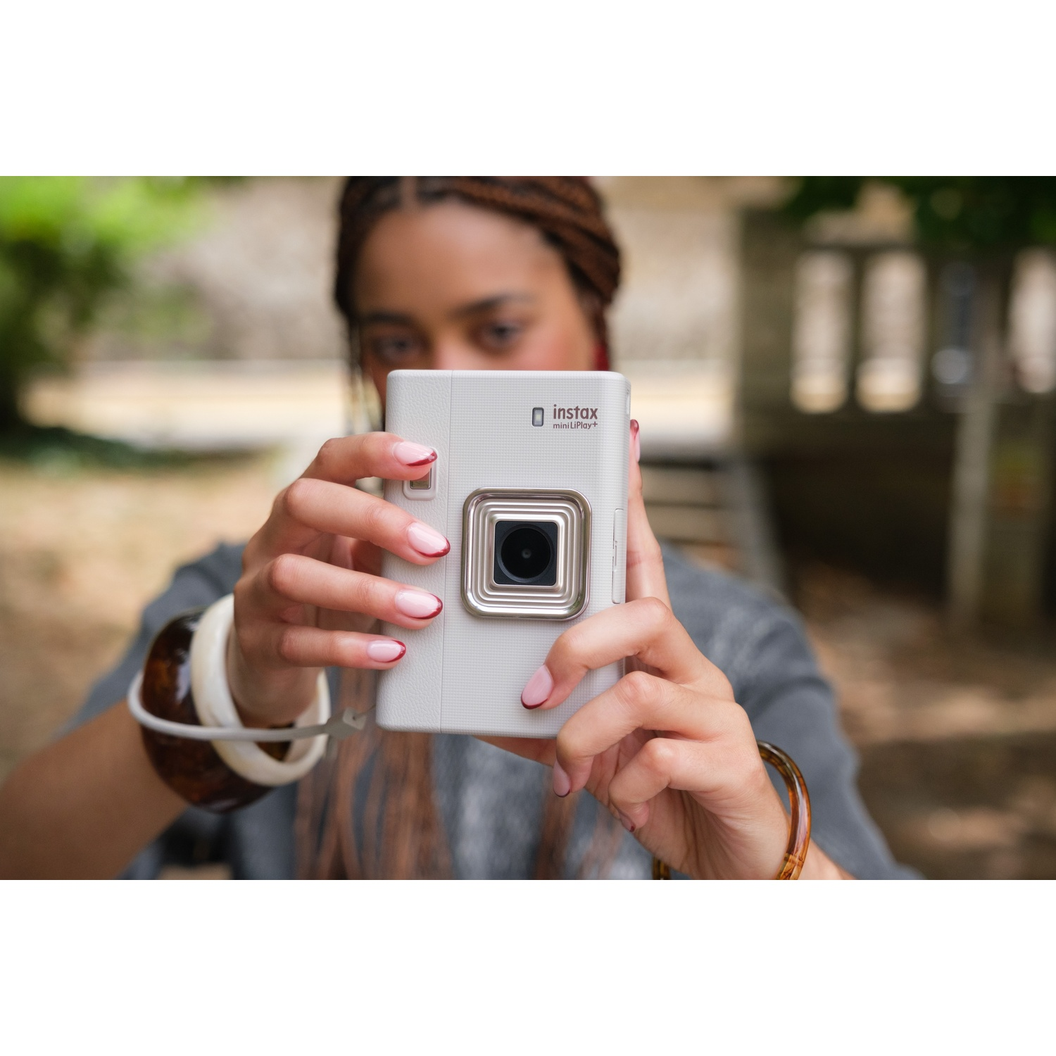 Une personne tient un appareil photo blanc Instax mini, avec un parc flou en arrière-plan.