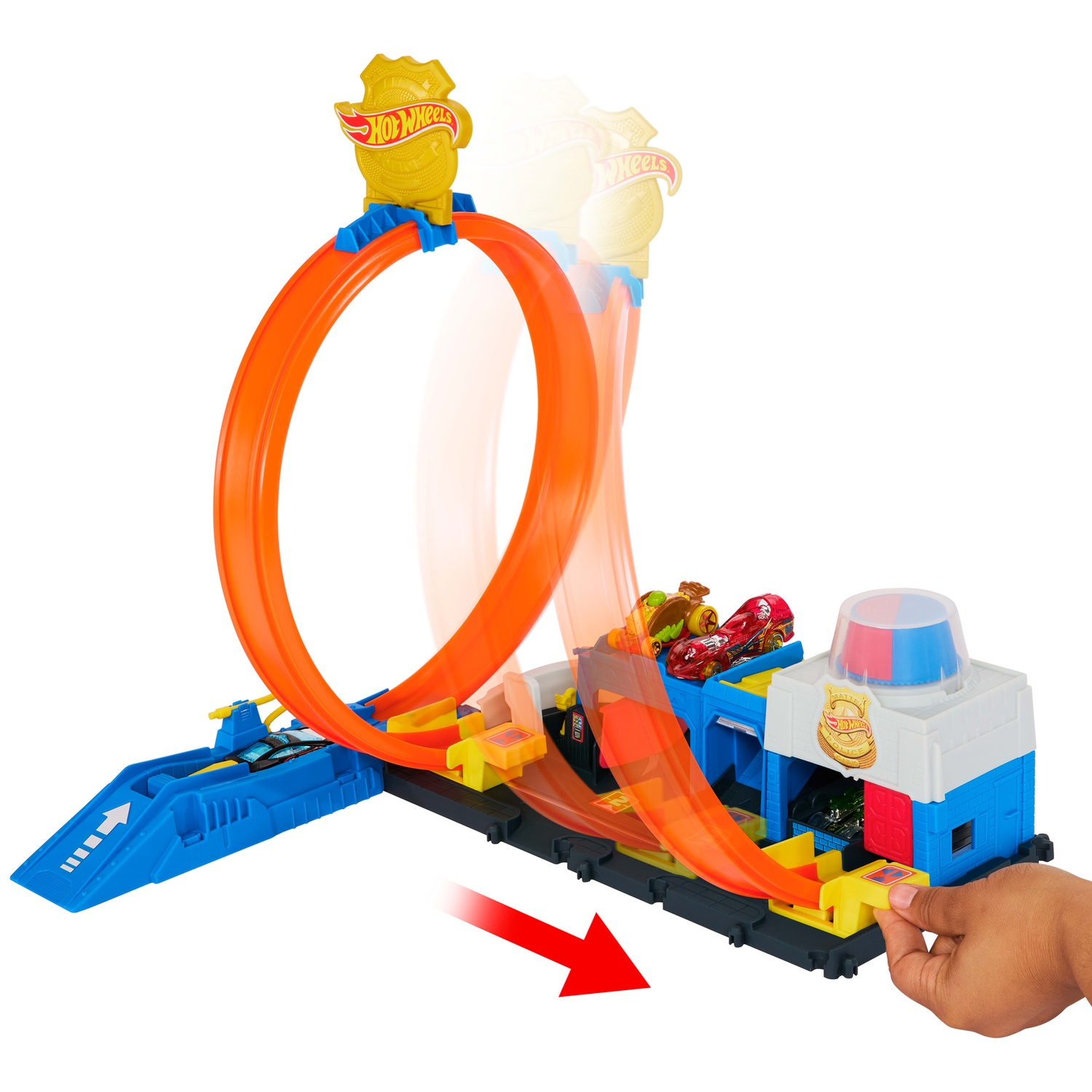 A Hot Wheels police station toy with an orange loop track and a hand adjusting it, with two toy cars on top.