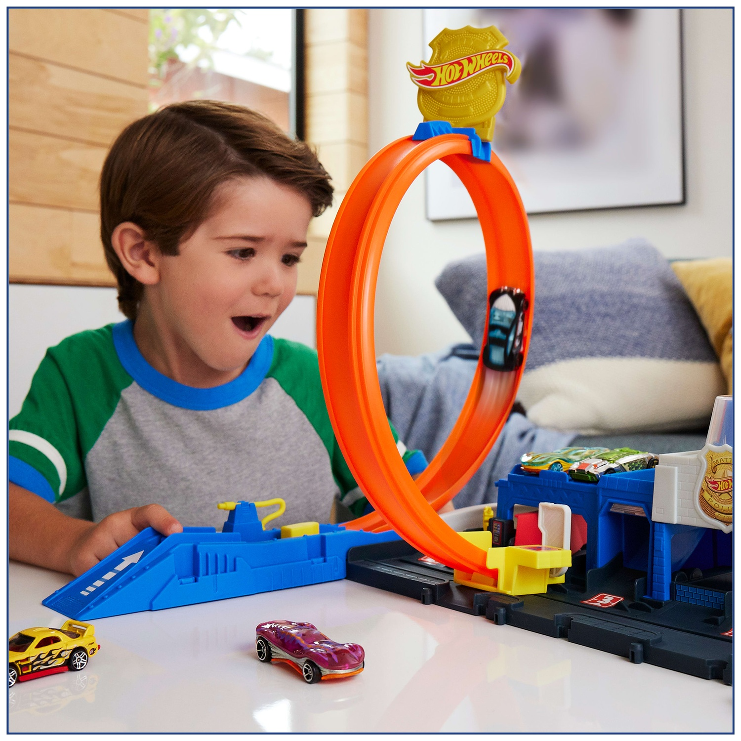 A boy looks amazed as a toy car races through an orange Hot Wheels loop track.