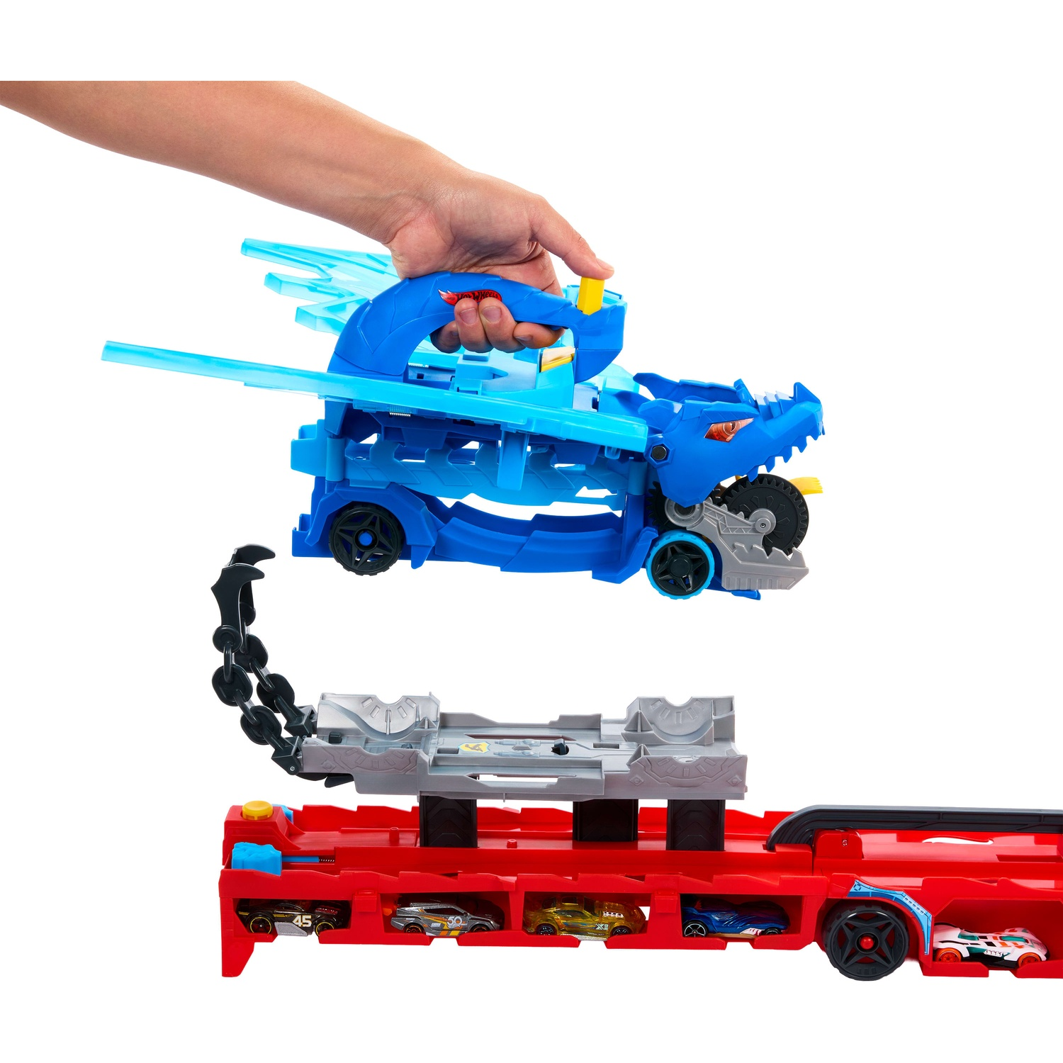 A hand holds a blue dragon toy above a red toy transporter holding smaller cars.