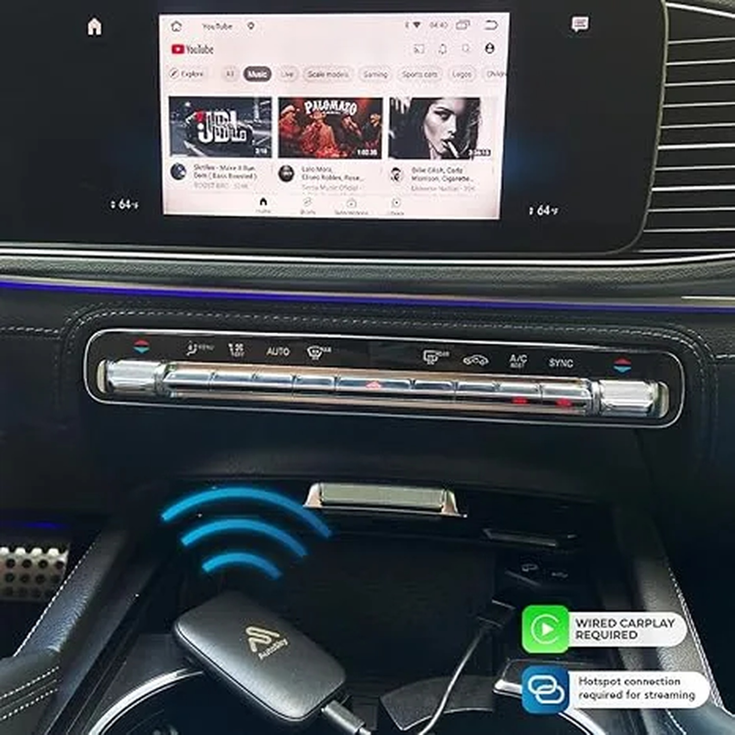 Een autodashboard touchscreen toont YouTube, met klimaatregeling eronder en een draadloze adapter.