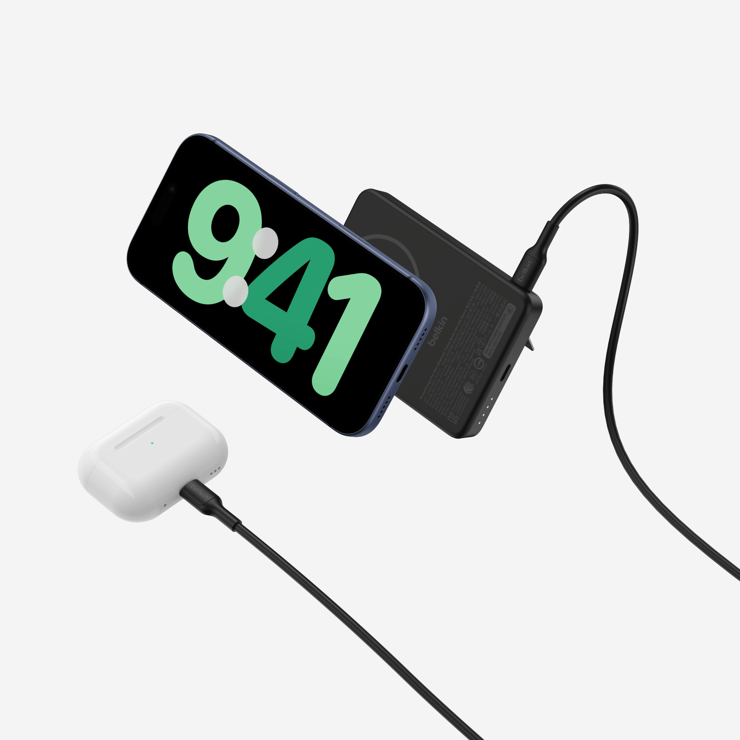 Un teléfono inteligente y un estuche de AirPods cargan en una superficie gris con cables conectados.