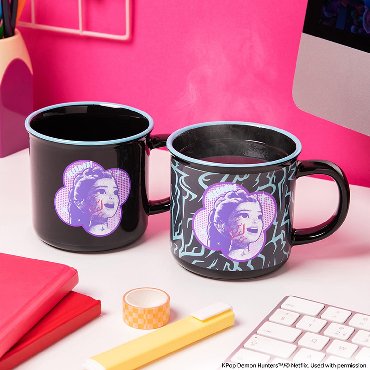 Deux tasses noires à bord bleu et portrait violet sont posées sur un bureau blanc sur fond rose.