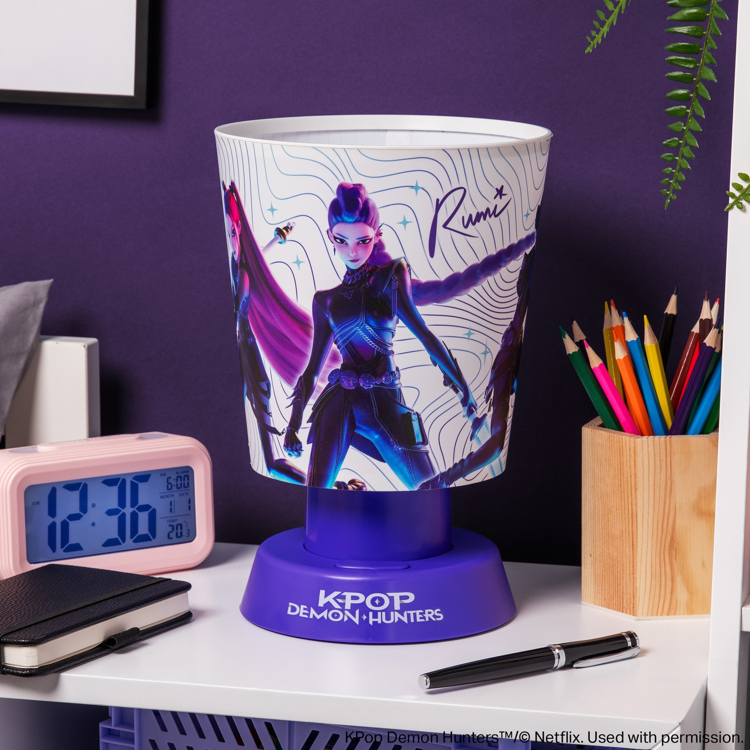 Une lampe violette KPop Demon Hunters sur un bureau avec une horloge rose et des crayons.