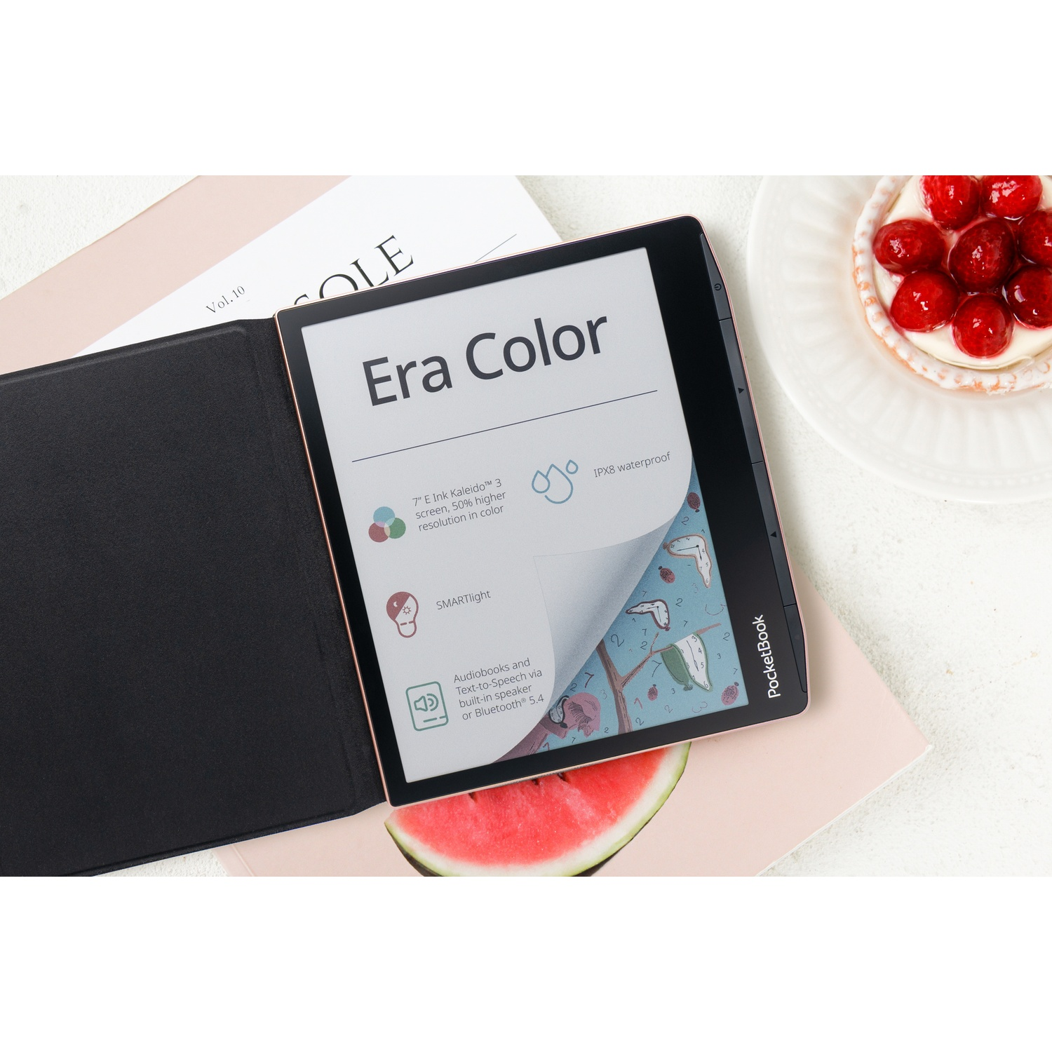 Een open PocketBook Era Color e-reader ligt op tijdschriften naast een bessen挞 en een watermeloen.