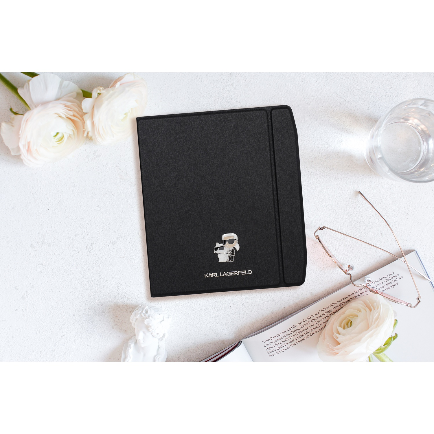 Zwarte Karl Lagerfeld tabletcover omringd door witte bloemen, een boek, een bril en een beeldje.