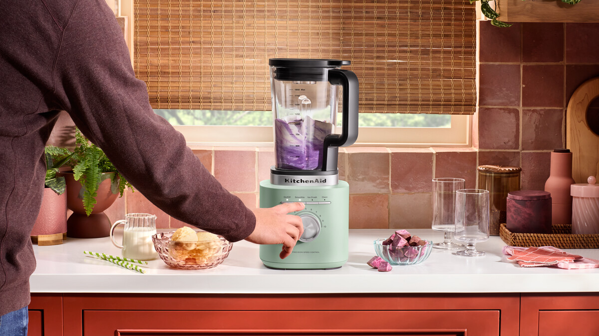 Person bedient einen pistaziengrünen KitchenAid-Mixer in einer Küche mit roten Fliesen.