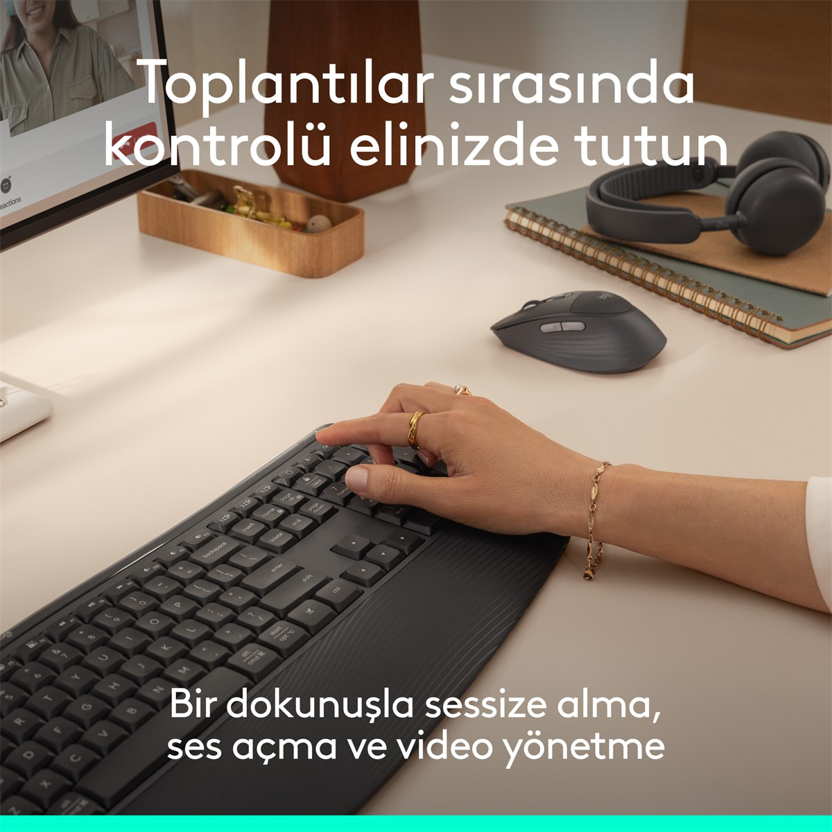 Fare, kulaklık ve monitör bulunan masada siyah klavyede yazan bir el.
