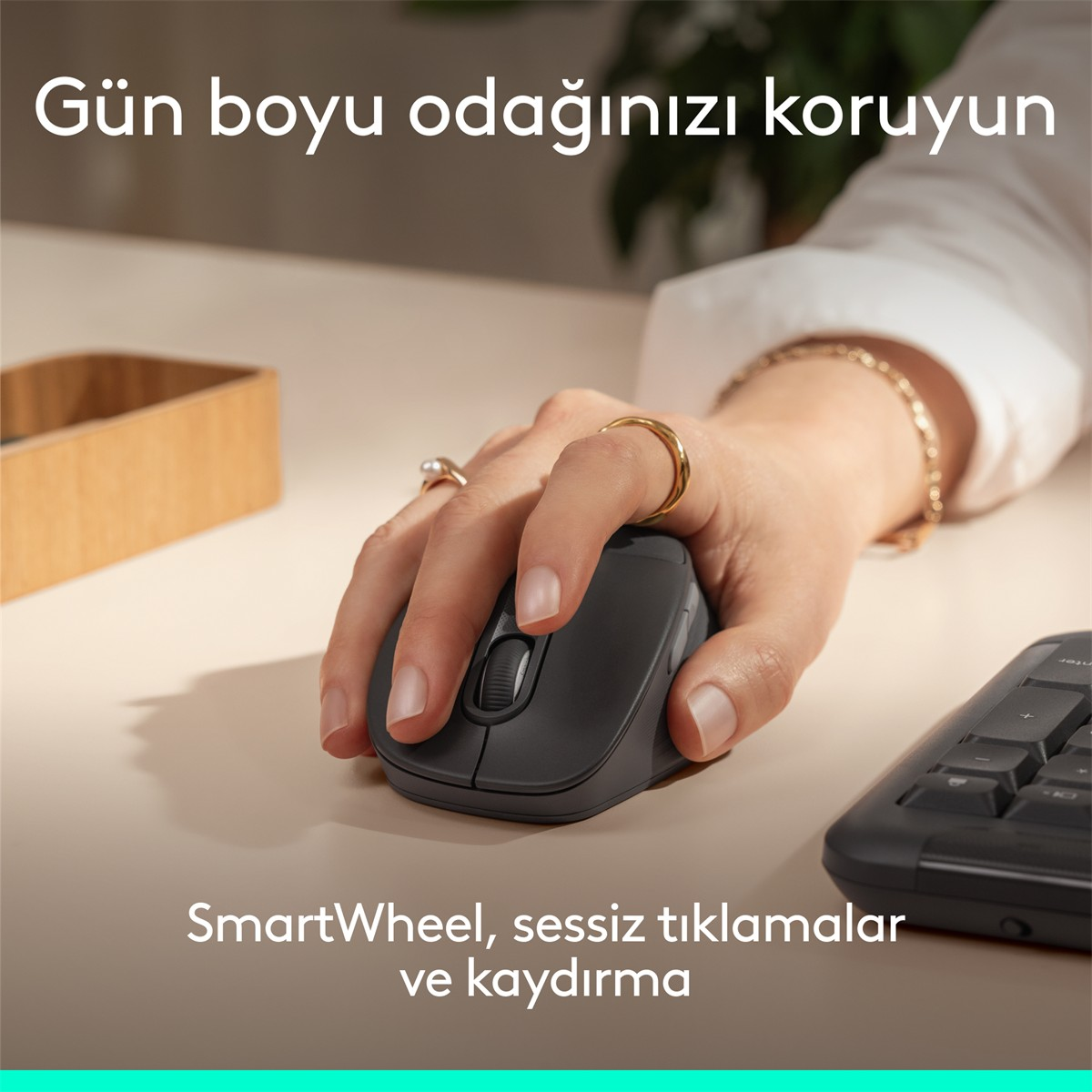 Bir el, klavyeli açık renkli masada gri bilgisayar faresini kullanıyor.