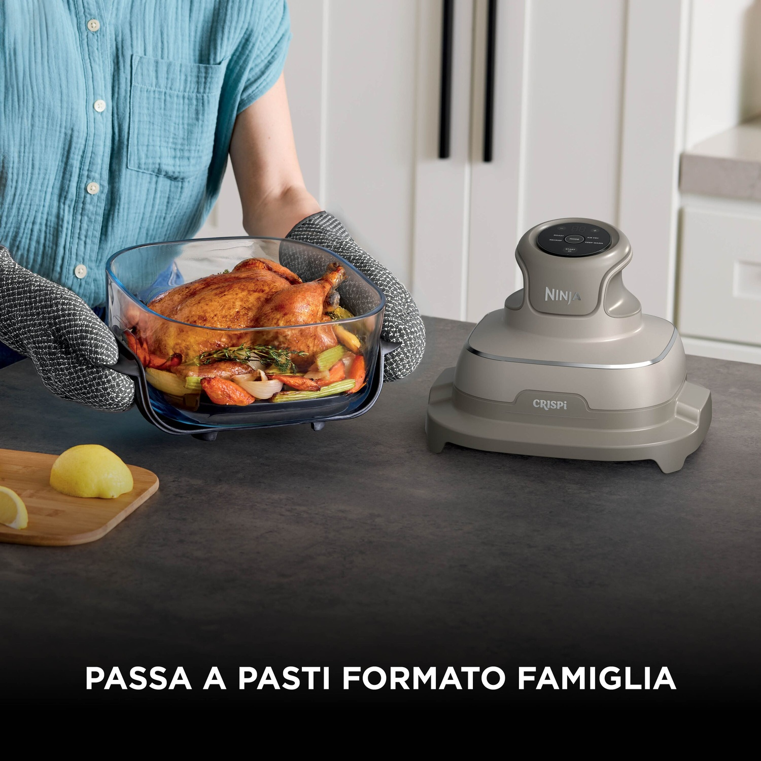 Una persona sostiene una teglia con pollo arrosto e verdure vicino a un elettrodomestico grigio.