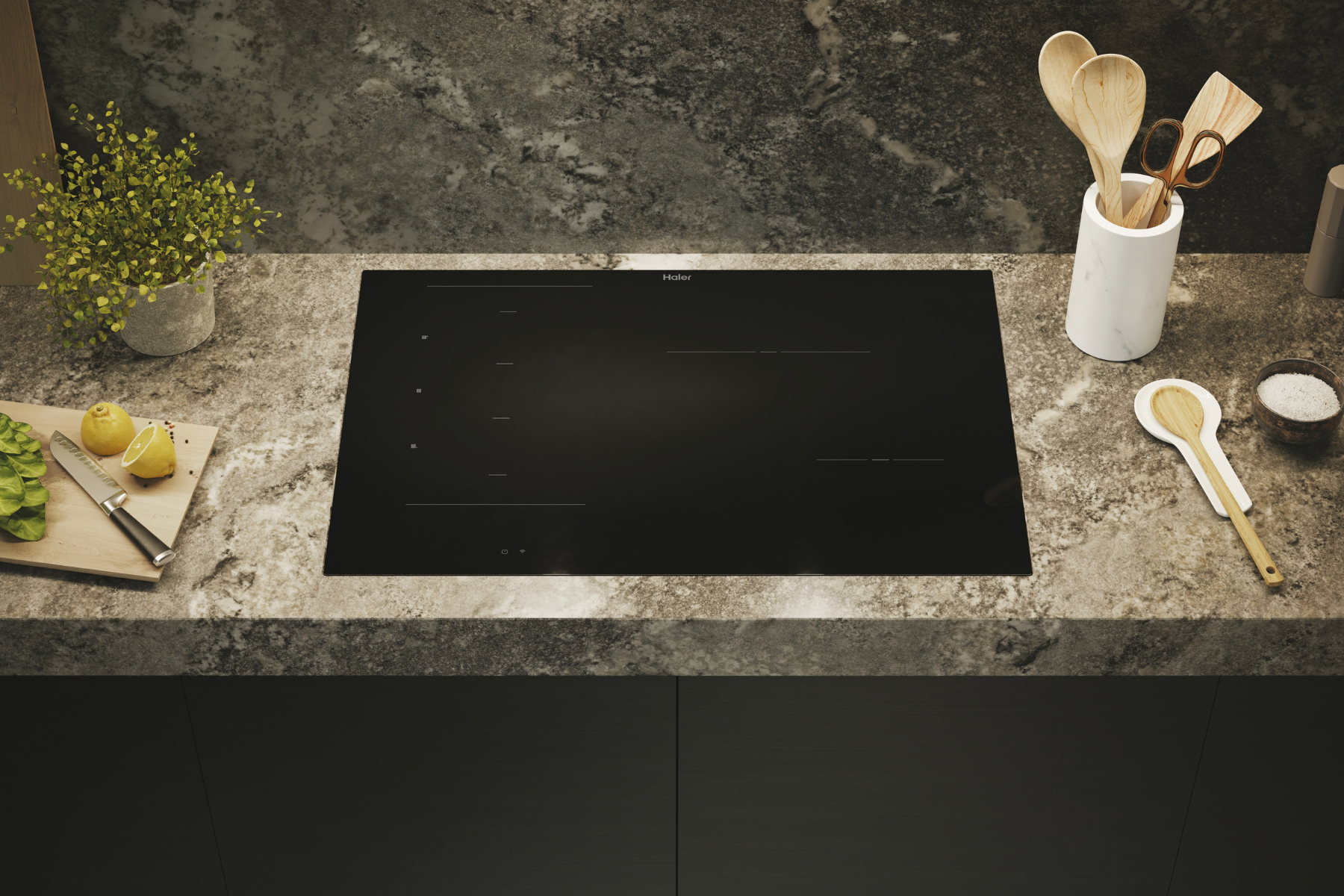 Placa de inducción Haier negra sobre encimera de mármol con utensilios, limones y hierbas.