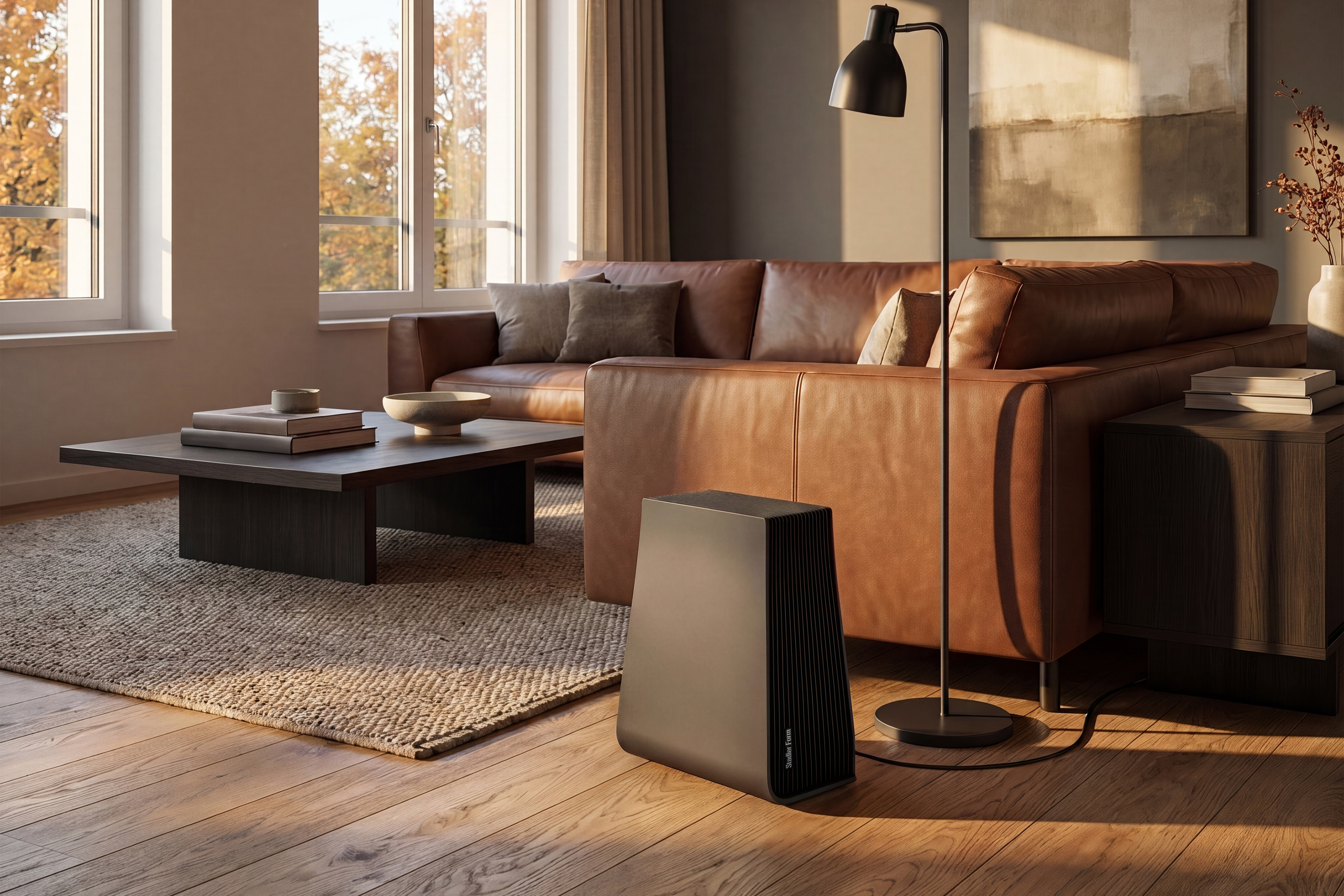 Ein schwarzer Luftreiniger steht auf einem Holzboden in einem warm beleuchteten Wohnzimmer mit braunem Ledersofa.