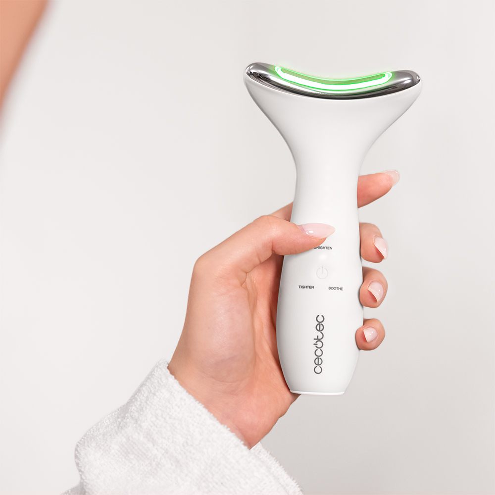 Una mano sostiene un dispositivo facial blanco y ergonómico con luz verde brillante.