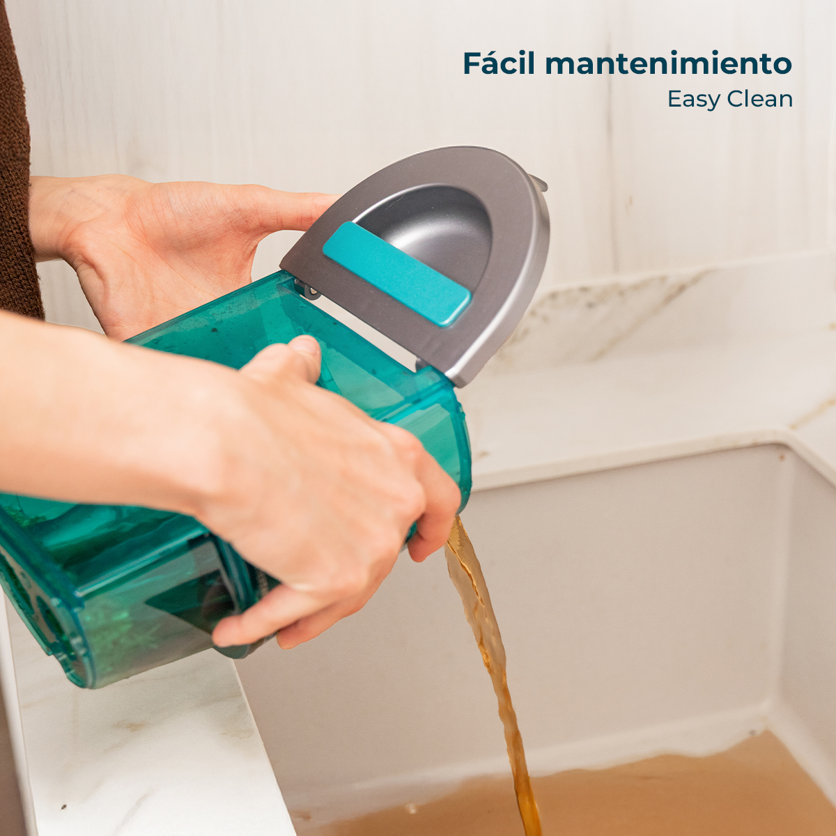Una persona vierte agua sucia de un tanque de mopa turquesa en un fregadero.