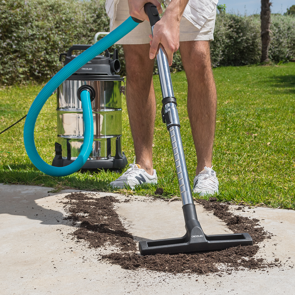 Un hombre usa una aspiradora industrial grande para aspirar tierra de una superficie de hormigón en el jardín.