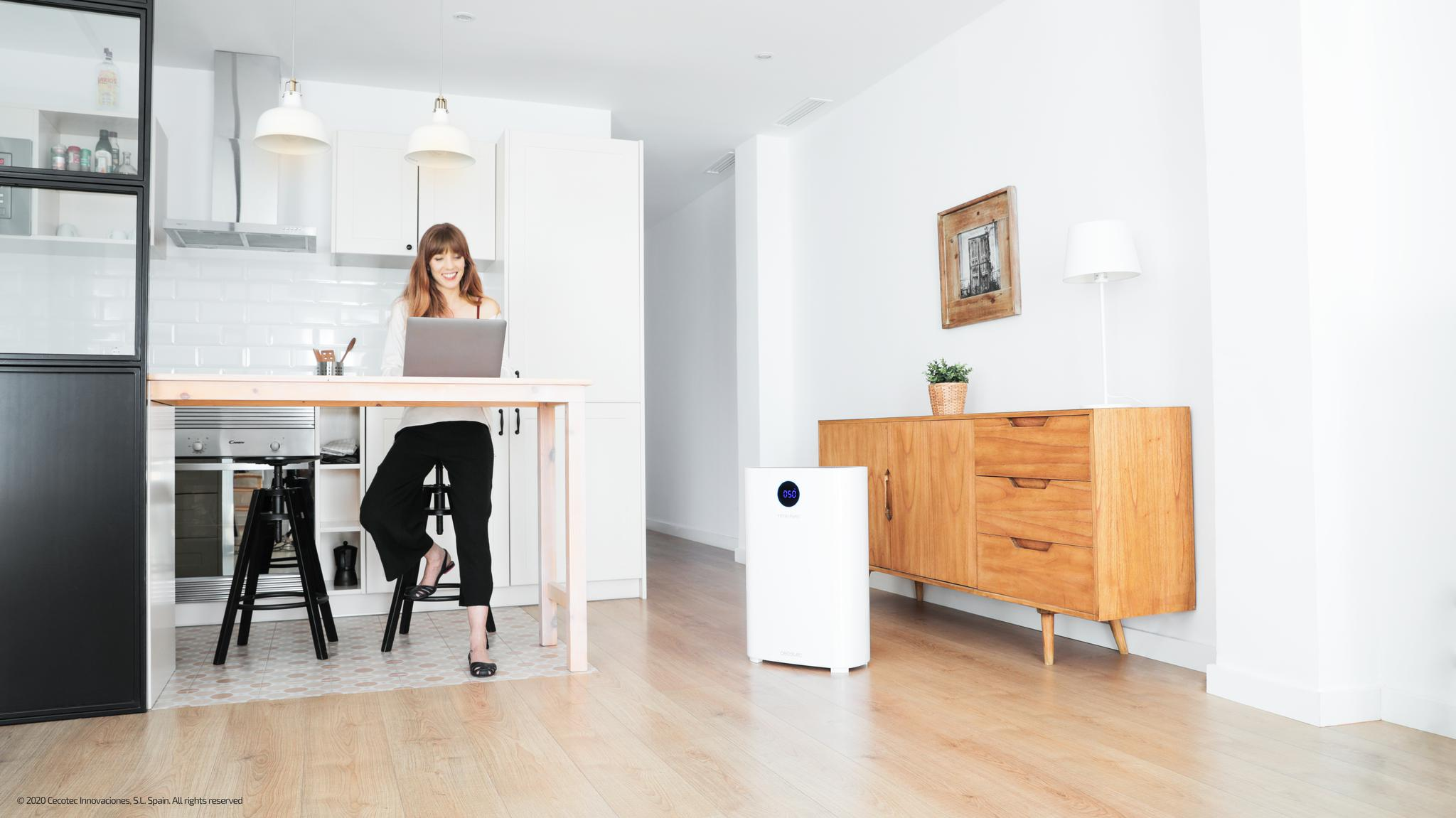 Mujer trabajando en portátil en mesa de madera en cocina luminosa con purificador.