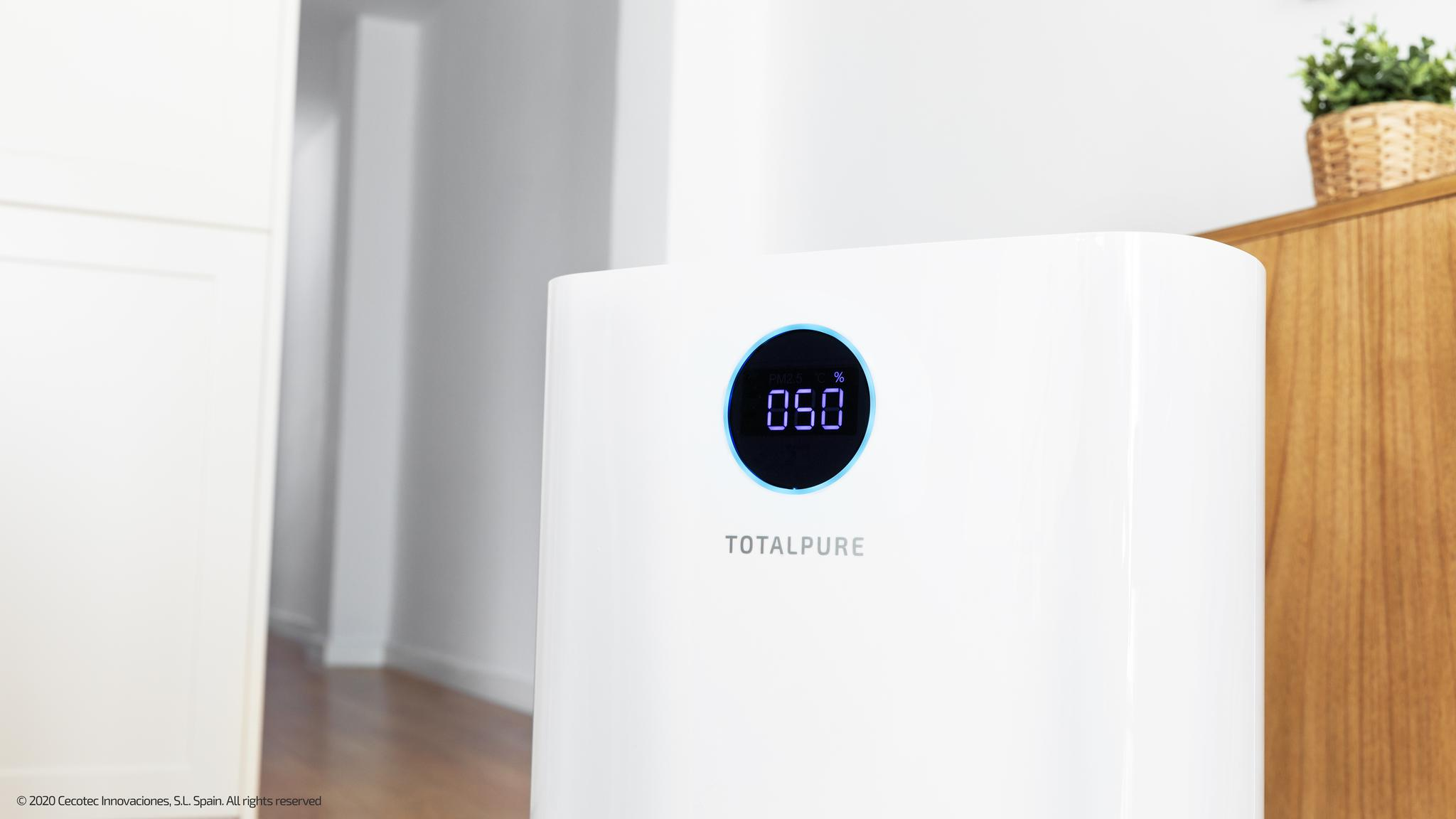 Un purificador de aire blanco Totalpure con pantalla LED azul en una habitación luminosa.