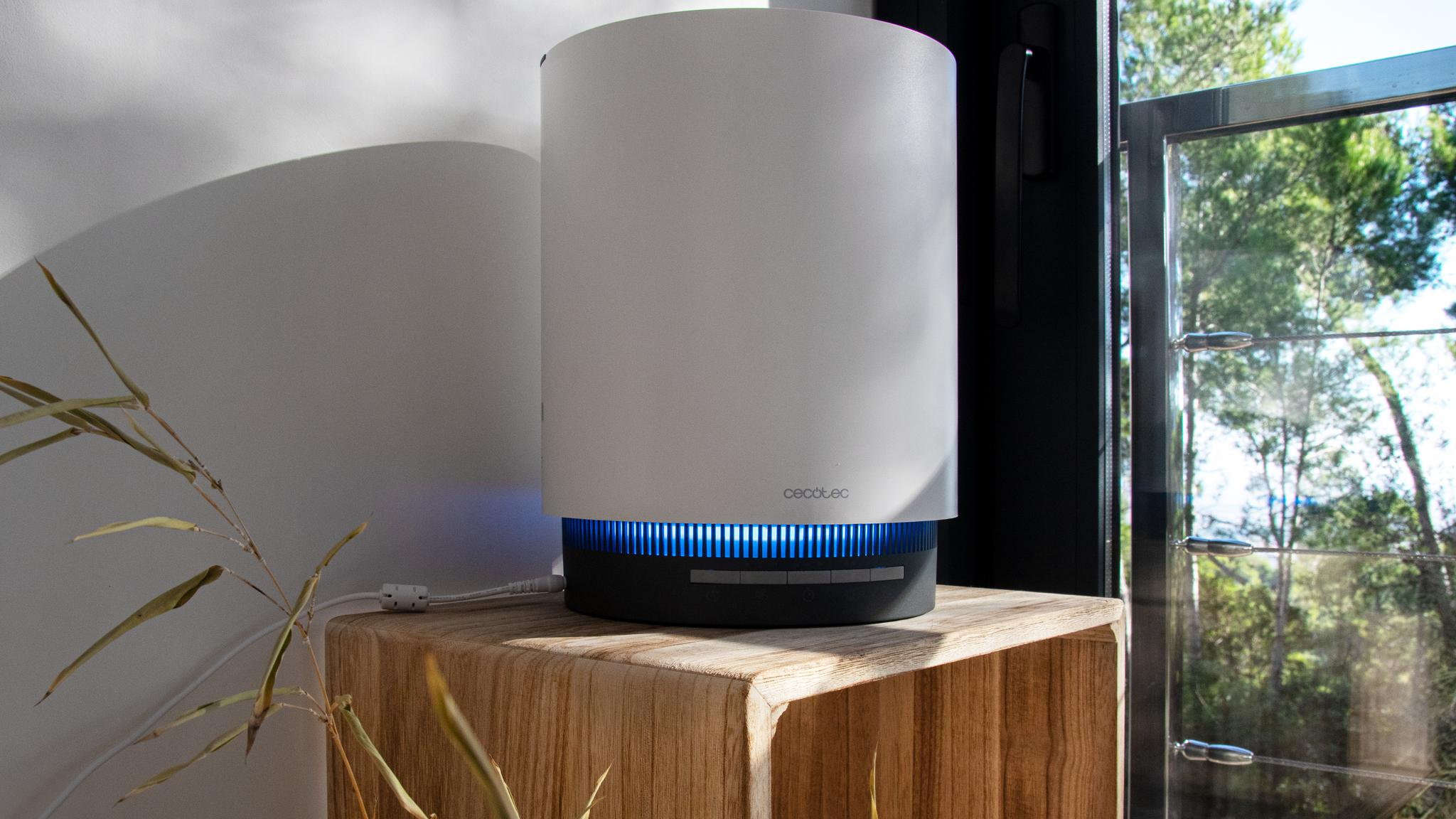 Un purificador de aire blanco con iluminación LED azul se encuentra sobre una mesa de madera.