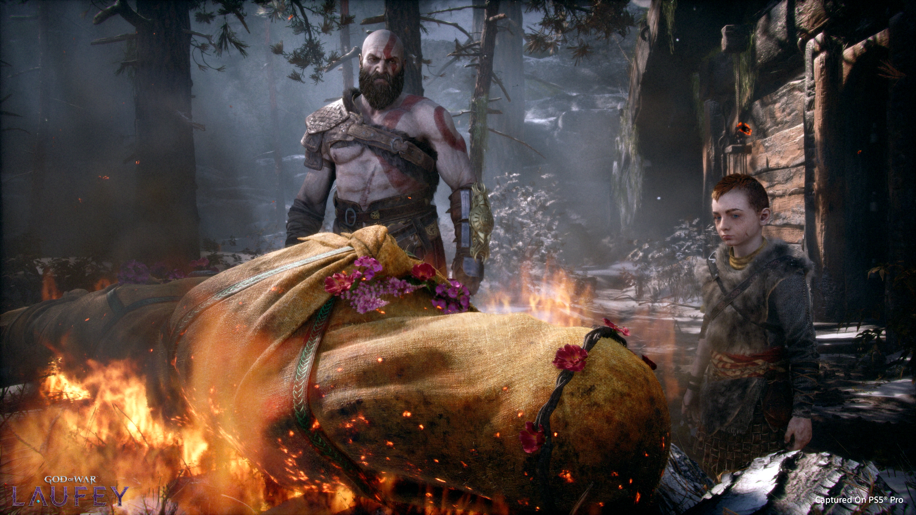 Kratos und Atreus stehen an einer brennenden Leiche in einem verschneiten Wald.