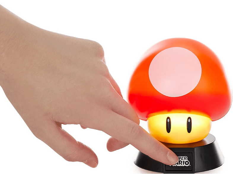 Una mano presiona el interruptor de una lámpara con forma de hongo de Super Mario sobre fondo blanco.
