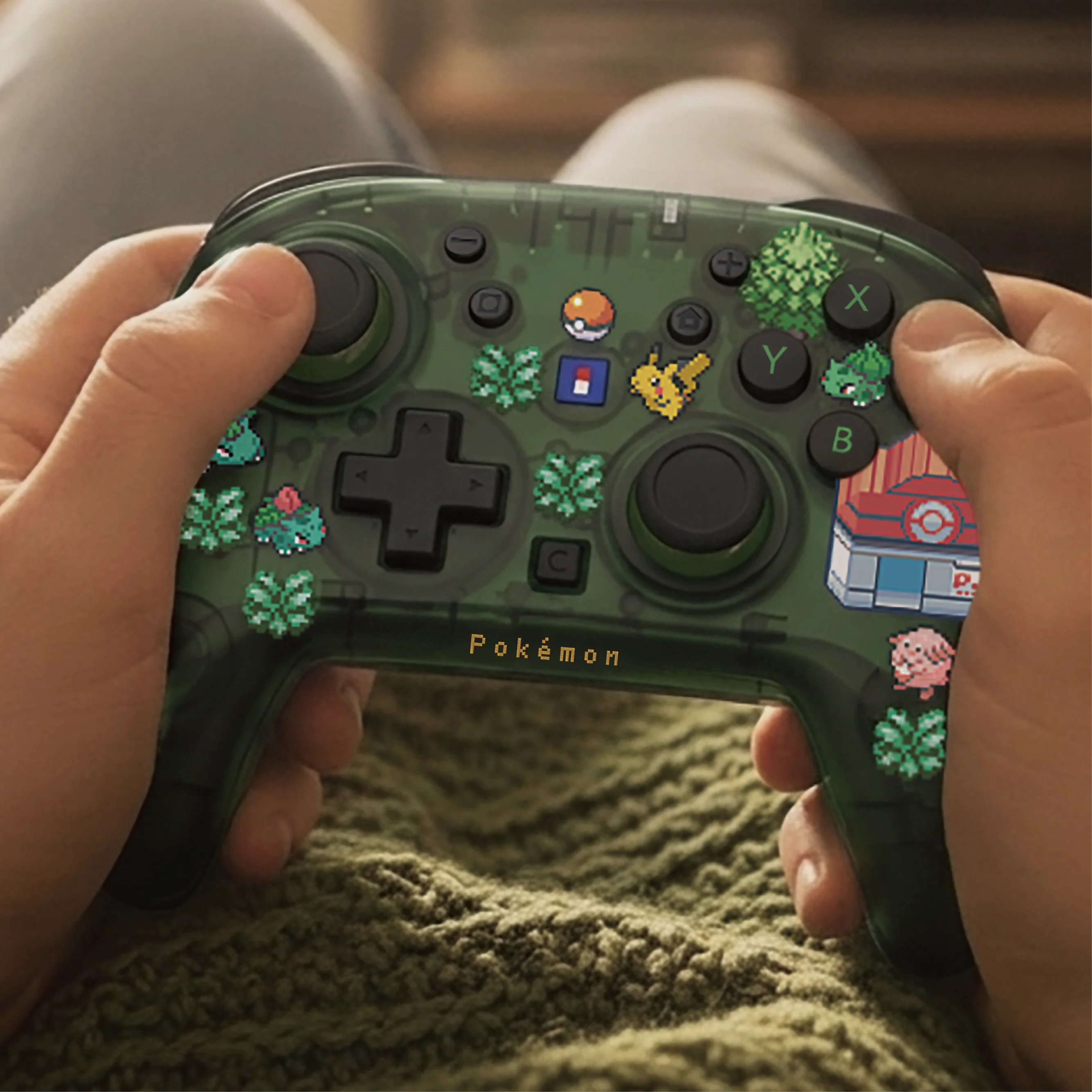 Una persona tiene in mano un controller per videogiochi Pokémon verde traslucido decorato con elementi in pixel art.