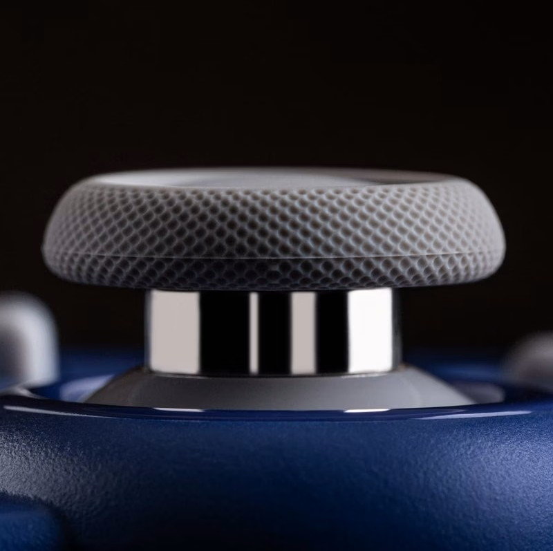 Primo piano di un joystick per gamepad grigio testurizzato su un corpo blu con sfondo nero.