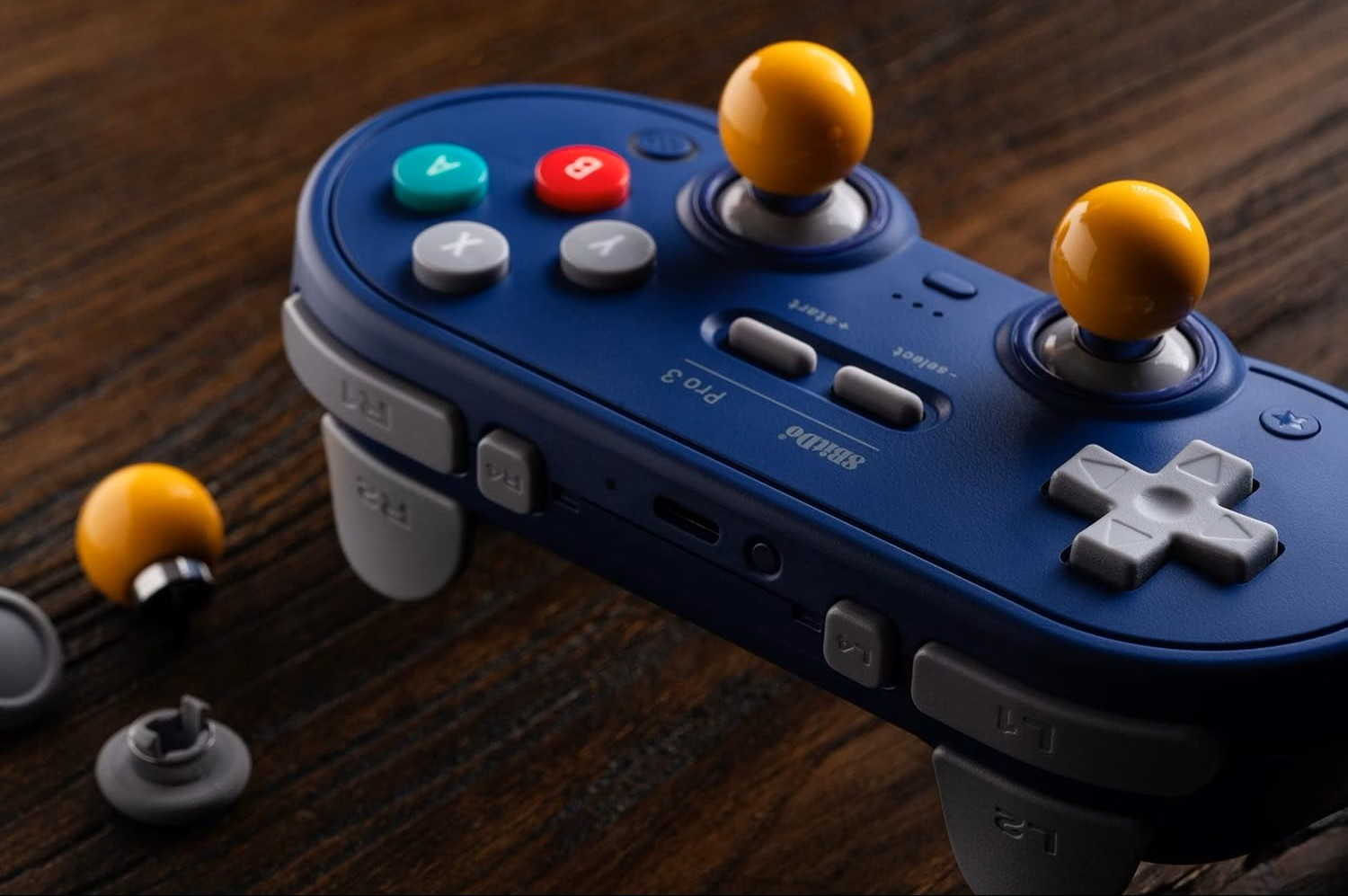 Un controller di gioco blu con levette gialle e pulsanti grigi si trova su una superficie in legno.