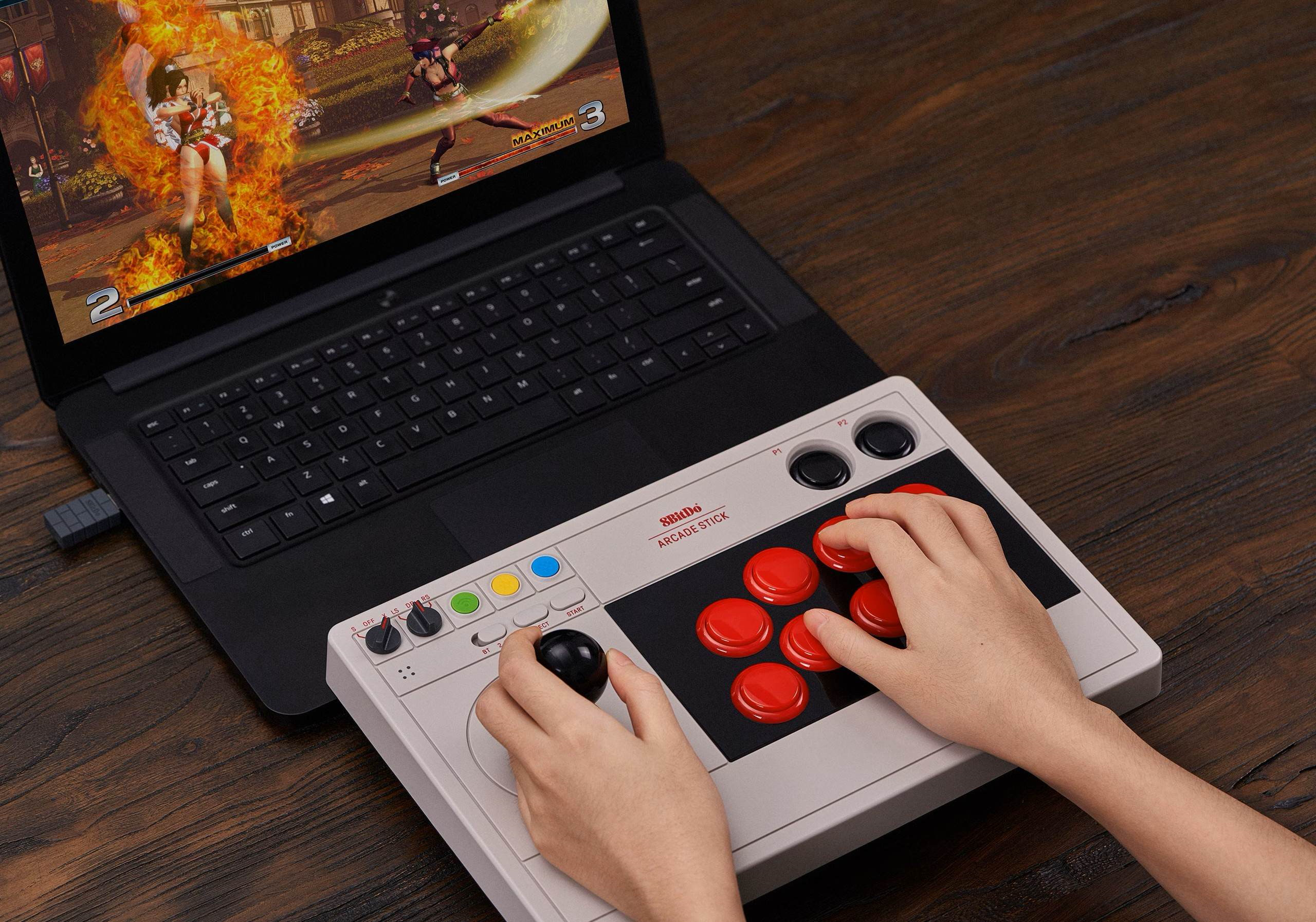 Un giocatore usa un joystick arcade grigio 8BitDo davanti a un laptop con un gioco di lotta.