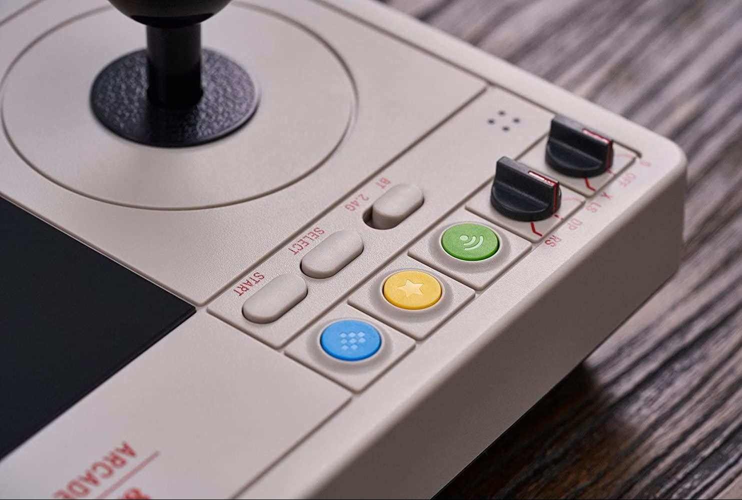 Primo piano di un controller arcade retro grigio con joystick, pulsanti colorati e interruttori.