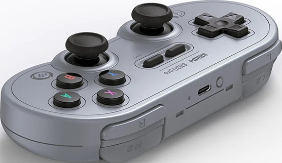 Controller di gioco retro grigio con due levette analogiche, D-pad, pulsanti colorati e trigger superiori.