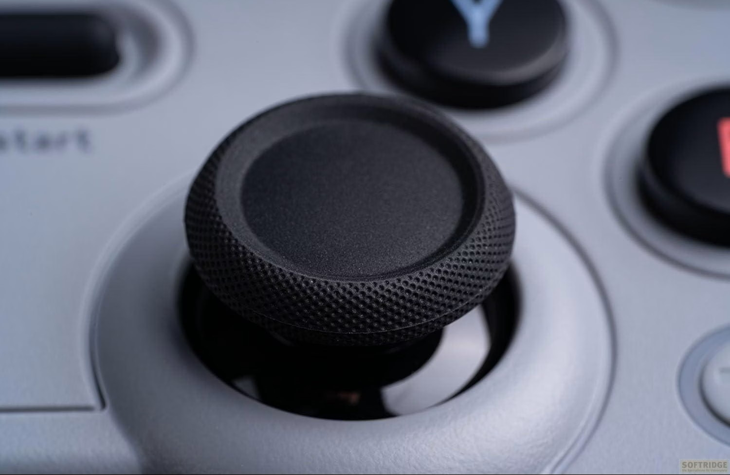 Primo piano di uno stick analogico nero su un controller grigio con pulsanti stampati sullo sfondo.