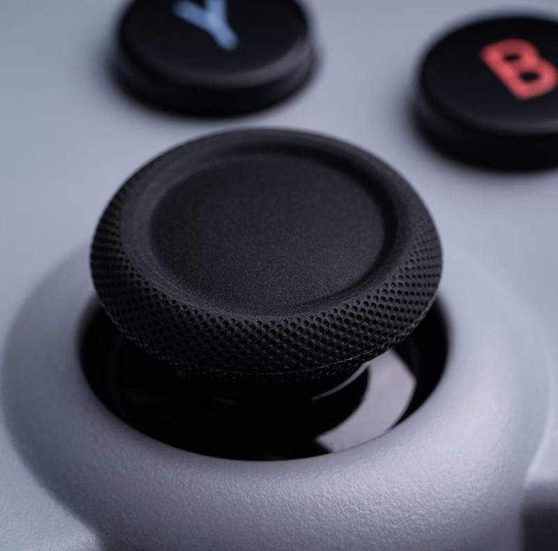 Primo piano di una levetta nera e pulsanti su un controller grigio.