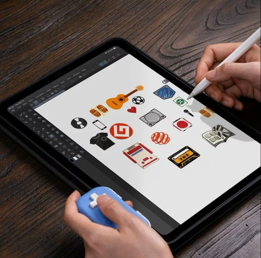 Una persona disegna icone digitali su un tablet con un pennino tenendo in mano un piccolo gamepad blu.