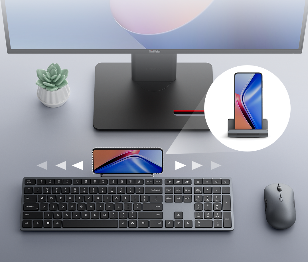 Teclado y ratón grises en el escritorio, con un smartphone en un soporte en la parte superior.