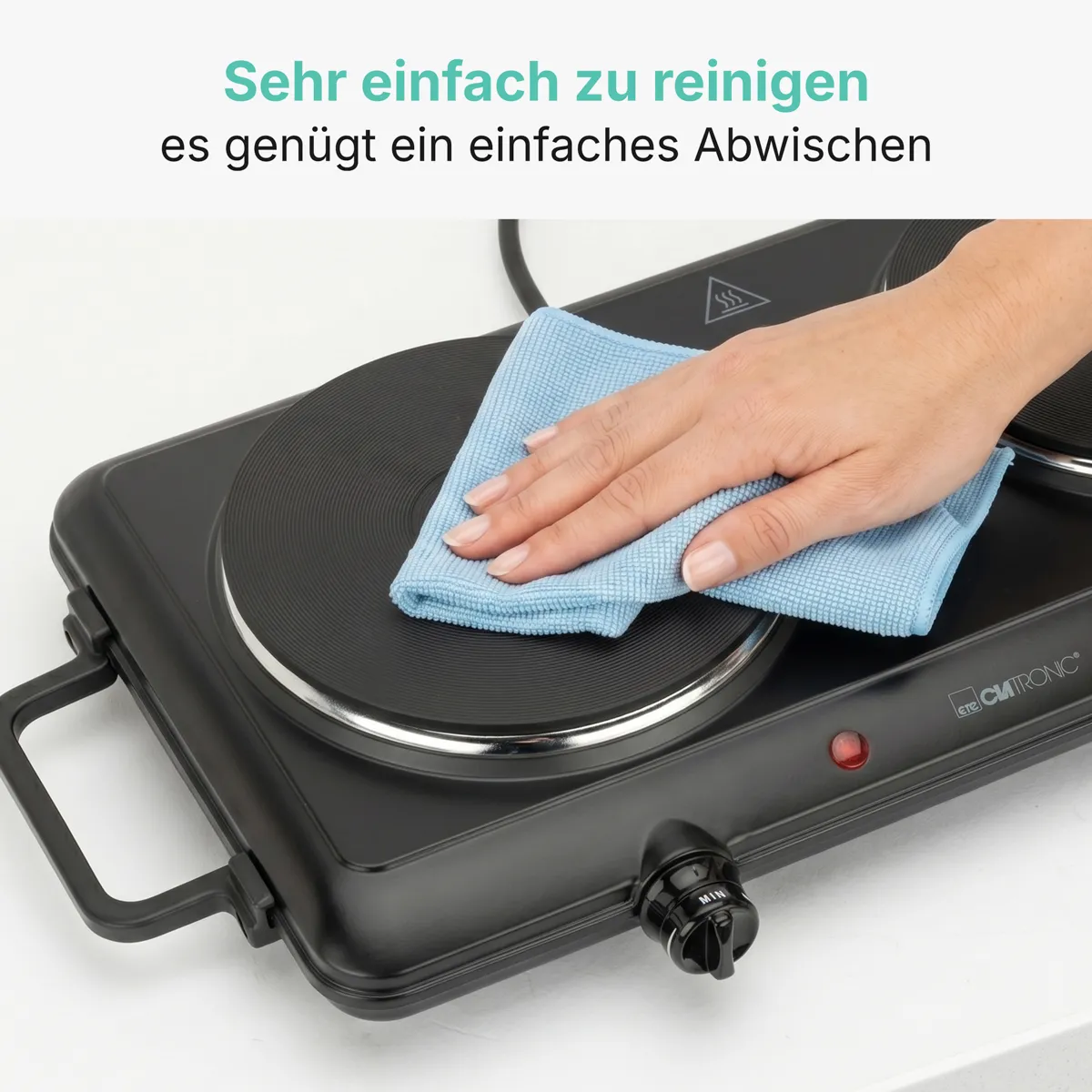 Eine Hand wischt mit einem blauen Tuch eine saubere schwarze Doppelkochplatte ab.