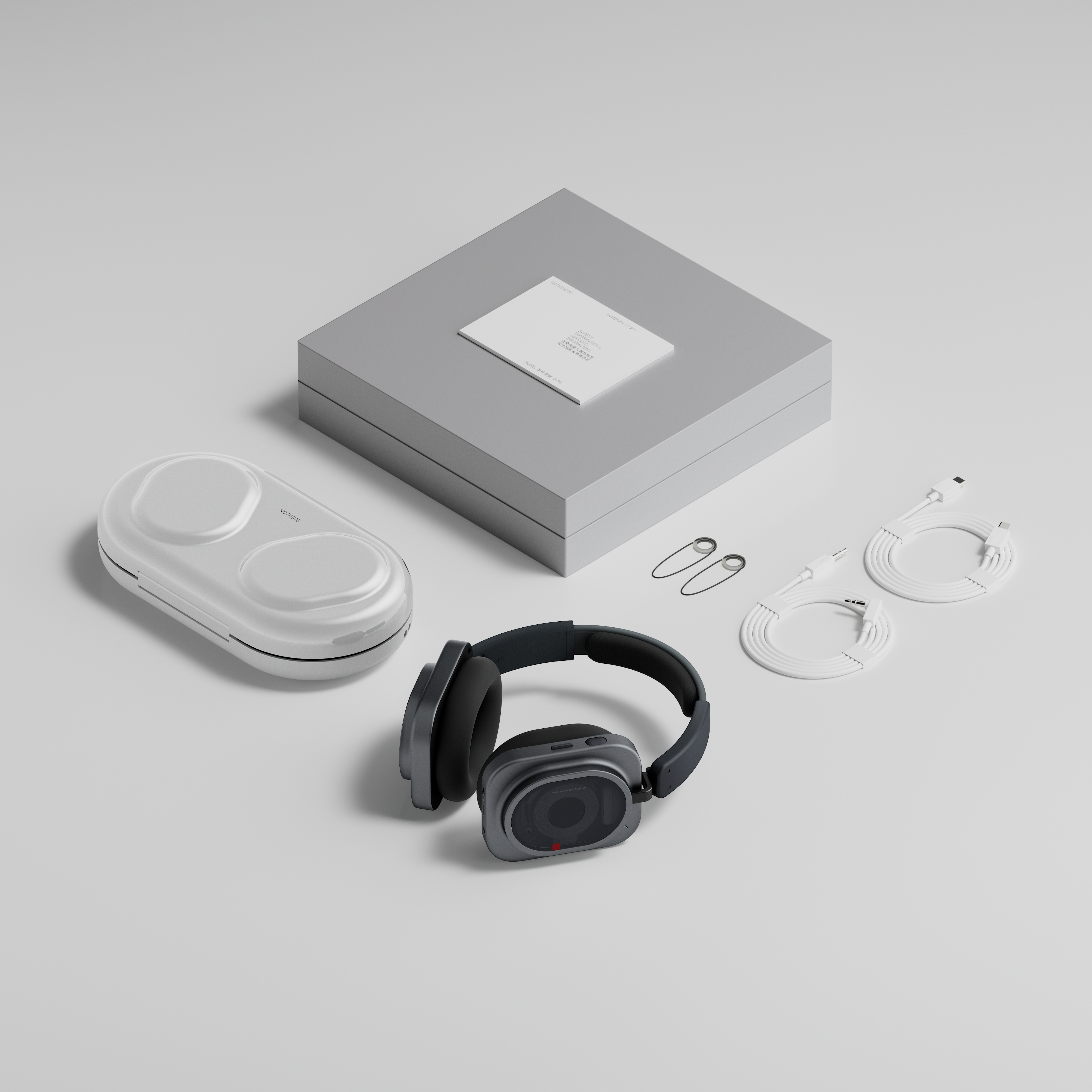 Graue Over-Ear-Kopfhörer, ein weißes Etui, Anleitungen, Kabel und kleines Zubehör auf einer grauen Oberfläche.